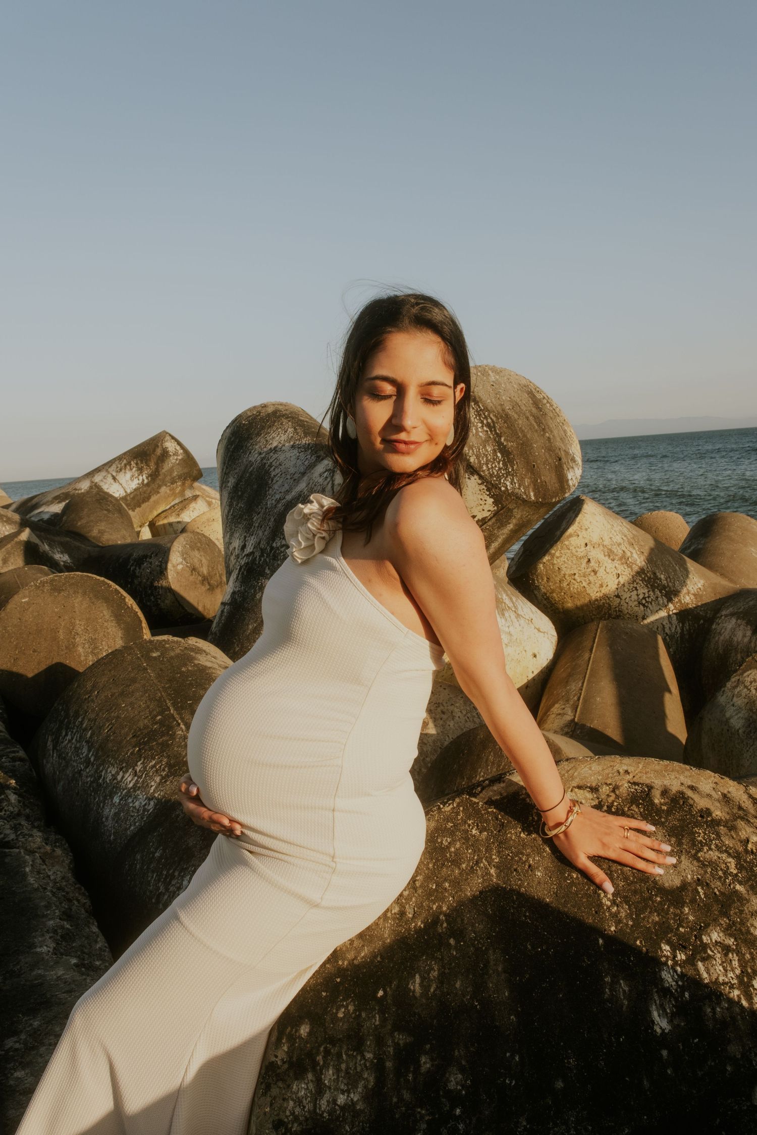 Maternity beach photoshoot on rocky shoreline during golden hour.