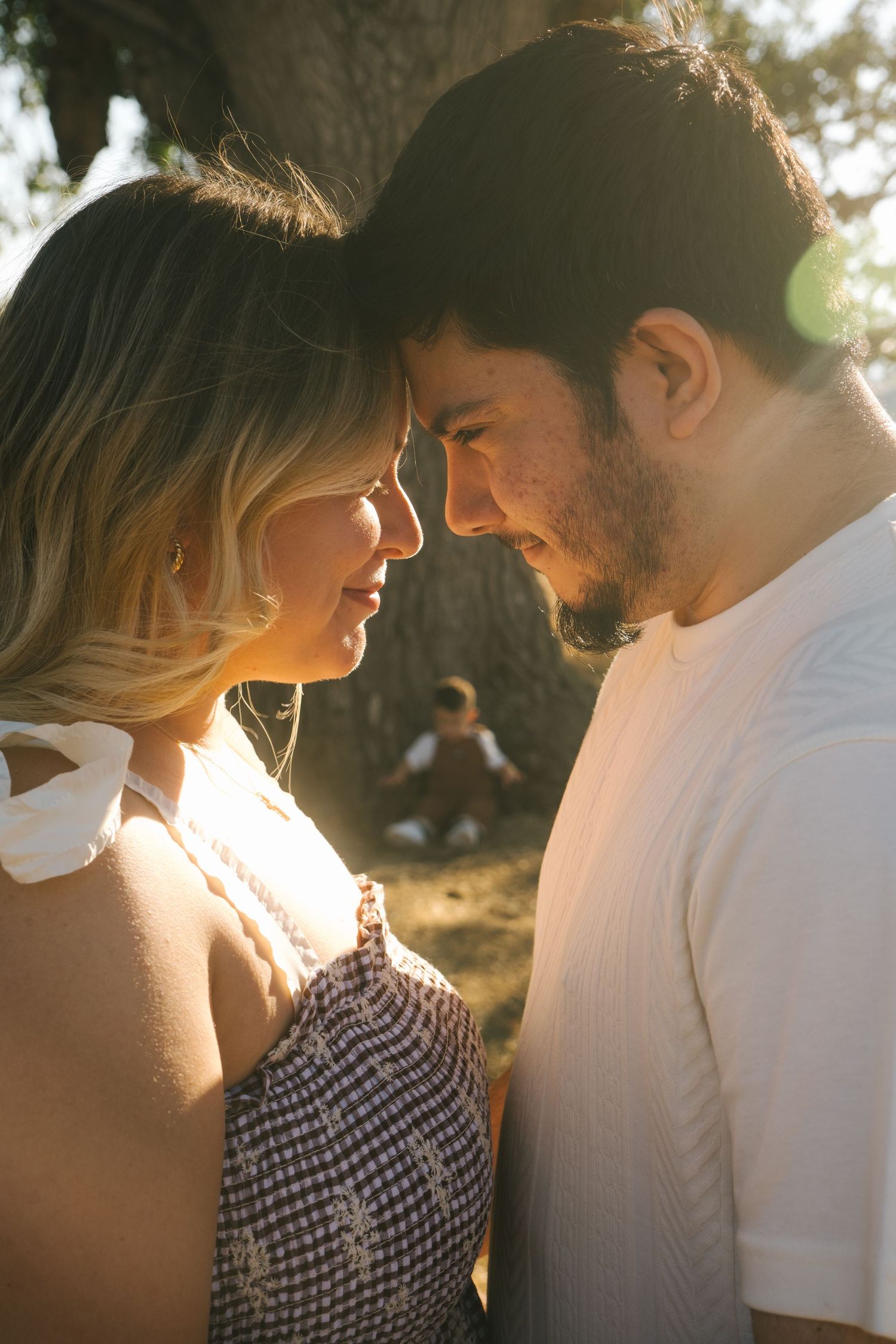 Romantic couple in white and gingham dress share intimate moment in golden sunlight.