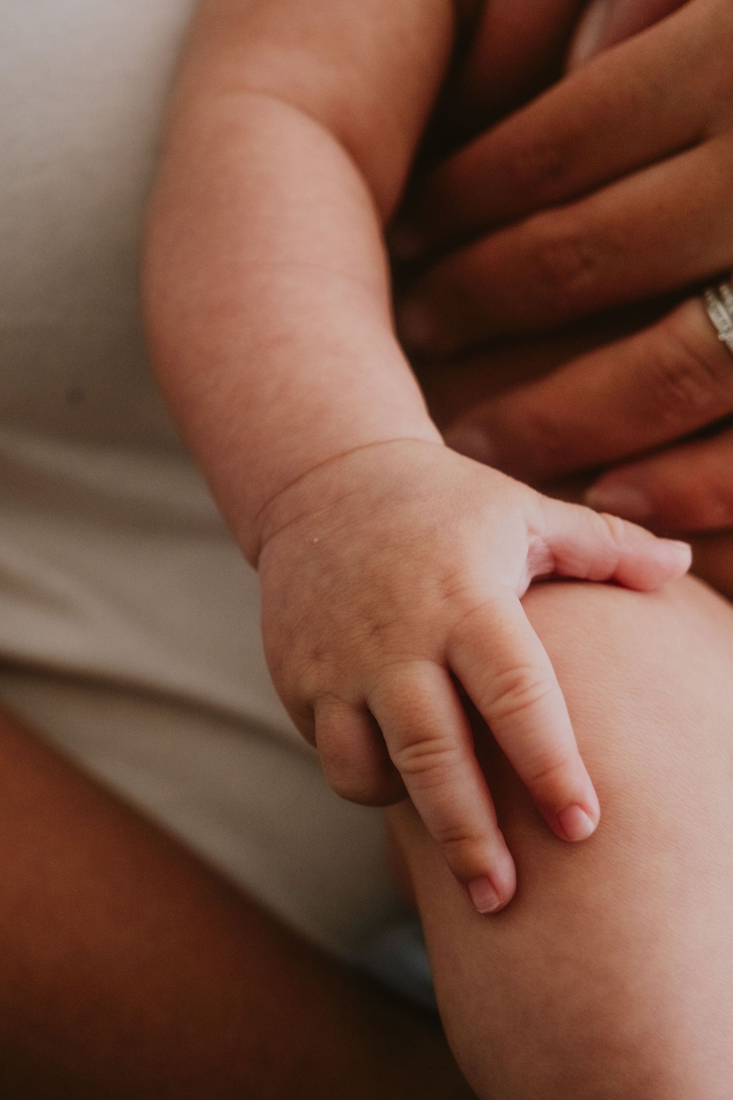 Gentle close-up of a baby's tiny hand resting on white fabric.