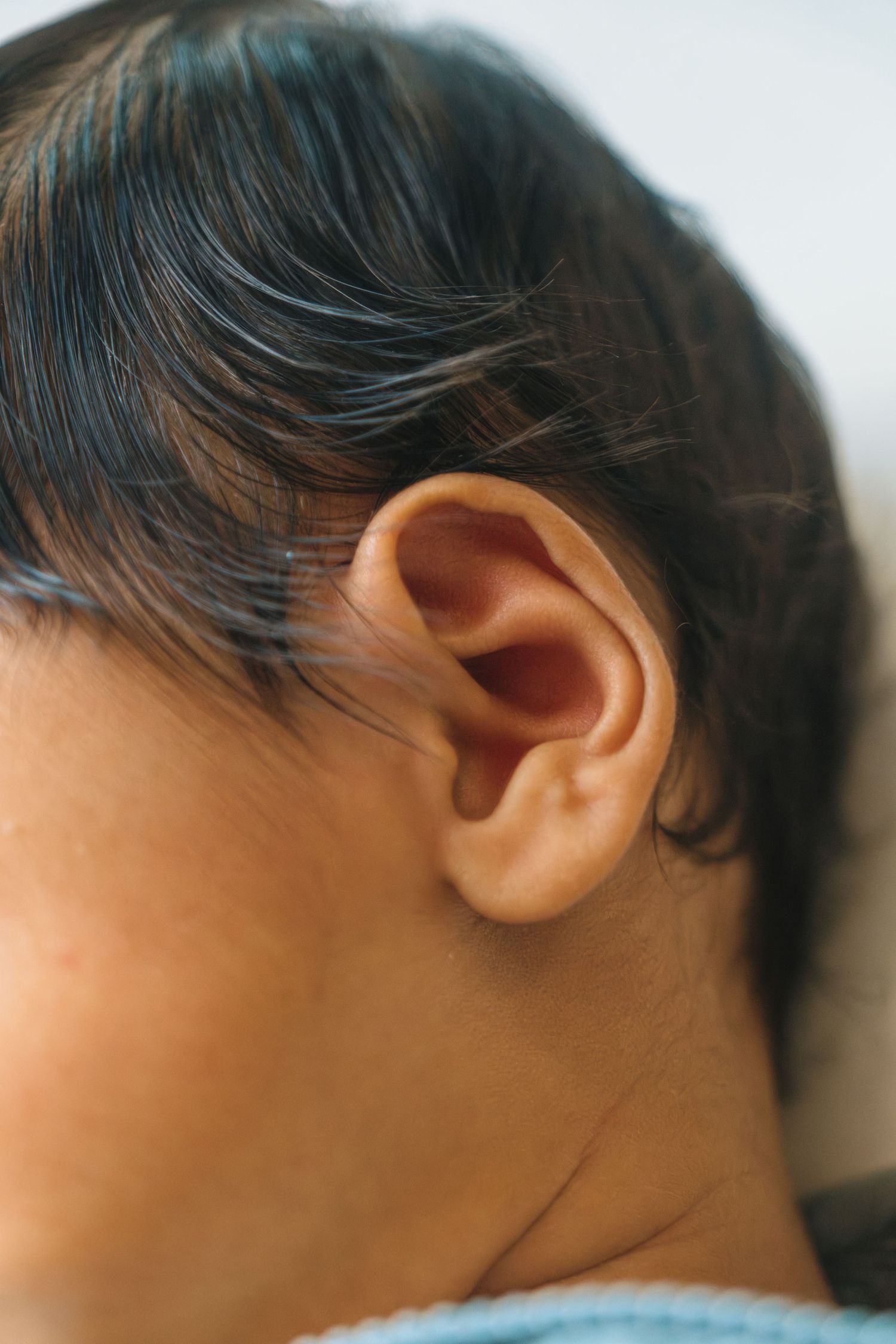 Close-up profile view of an ear and dark hair against a light background.