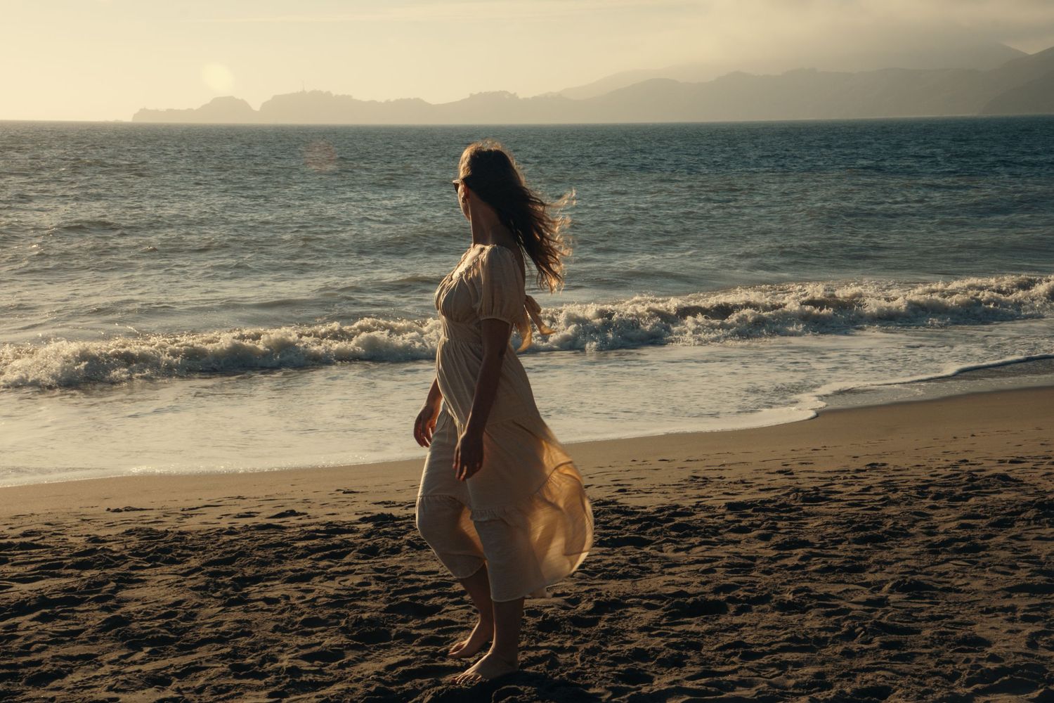 Silhouetted figures walking along beach at sunset with waves crashing.
