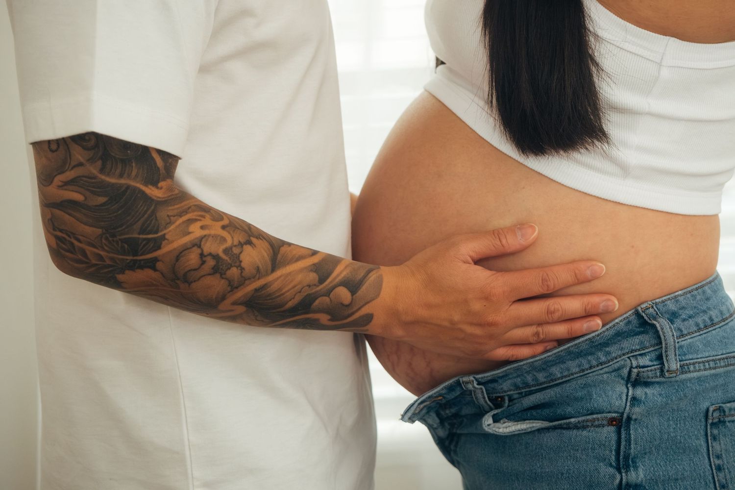 Close up of couple embracing, showing tattooed arm and denim jeans.