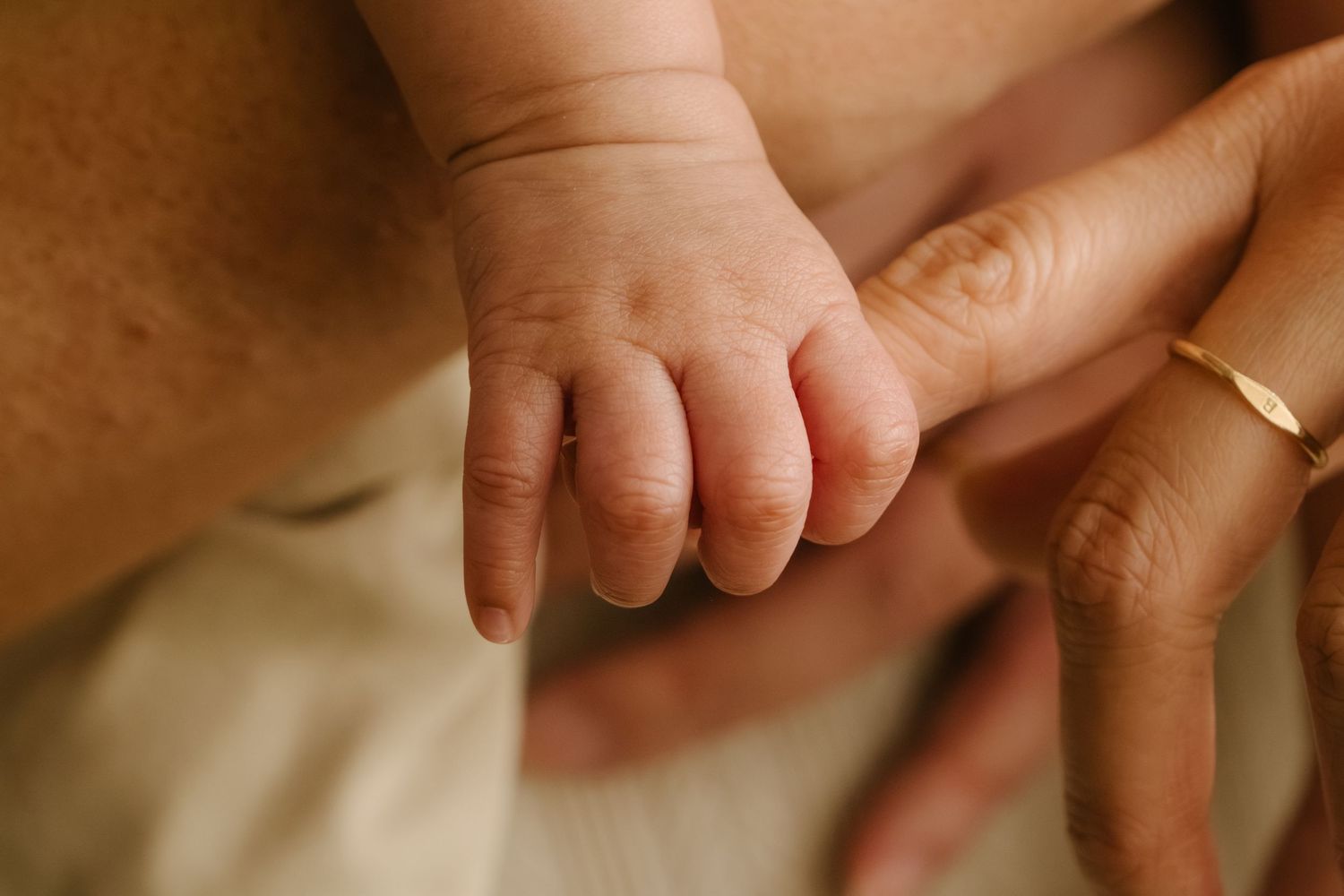 Close-up of infant hands and feet with adult hands providing gentle support.