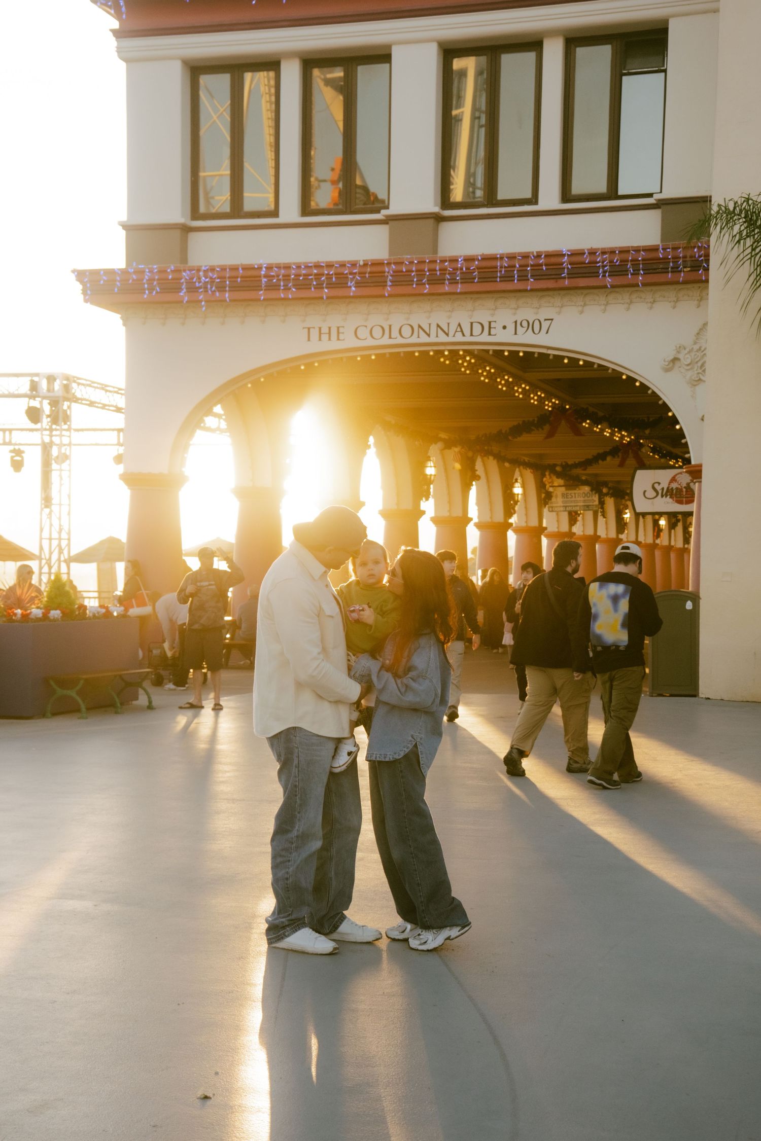 Couple embracing at golden hour outside The Colonnade 1907 building on a busy waterfront promenade.