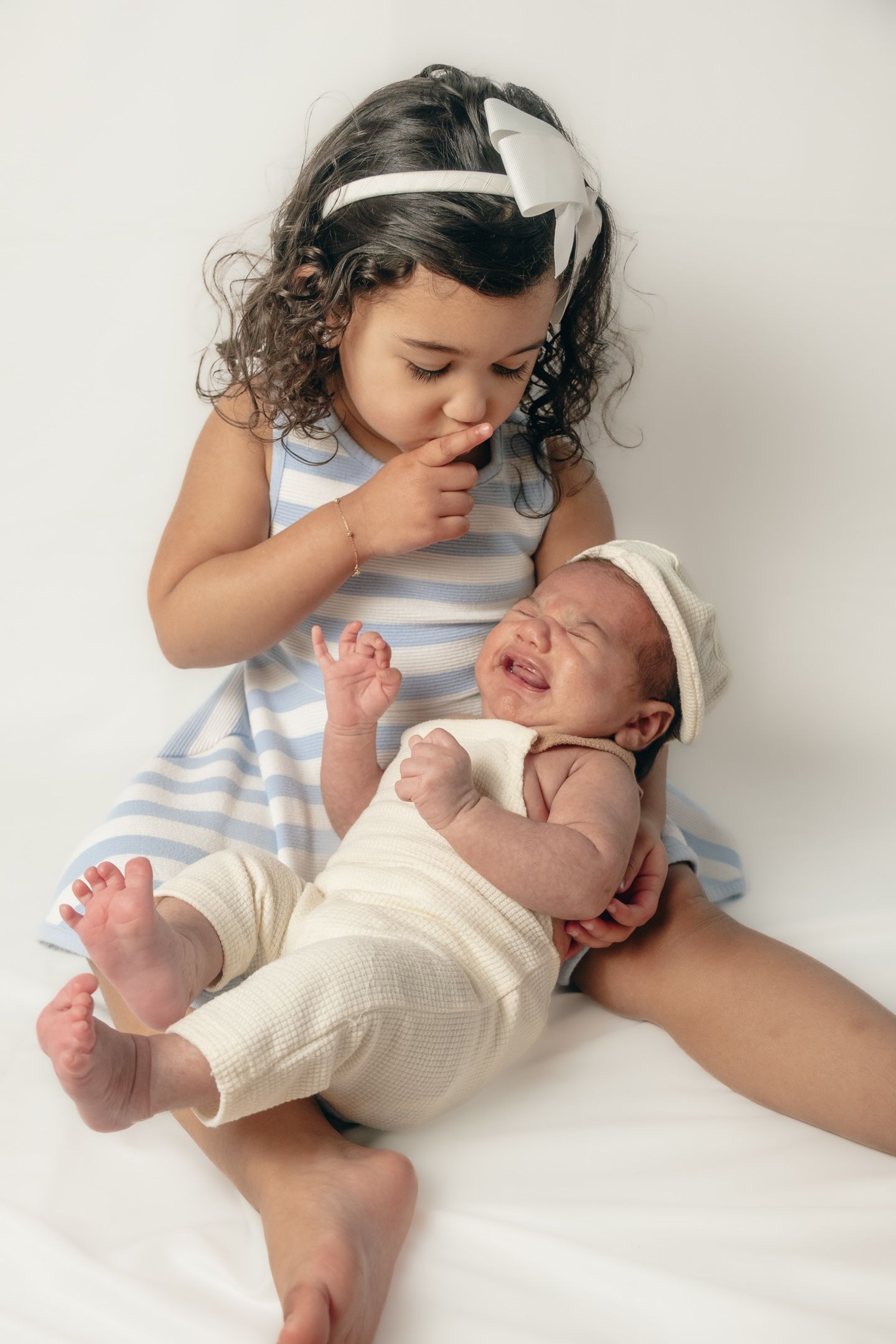 Baby in white onesie lying on white surface during tender moment.