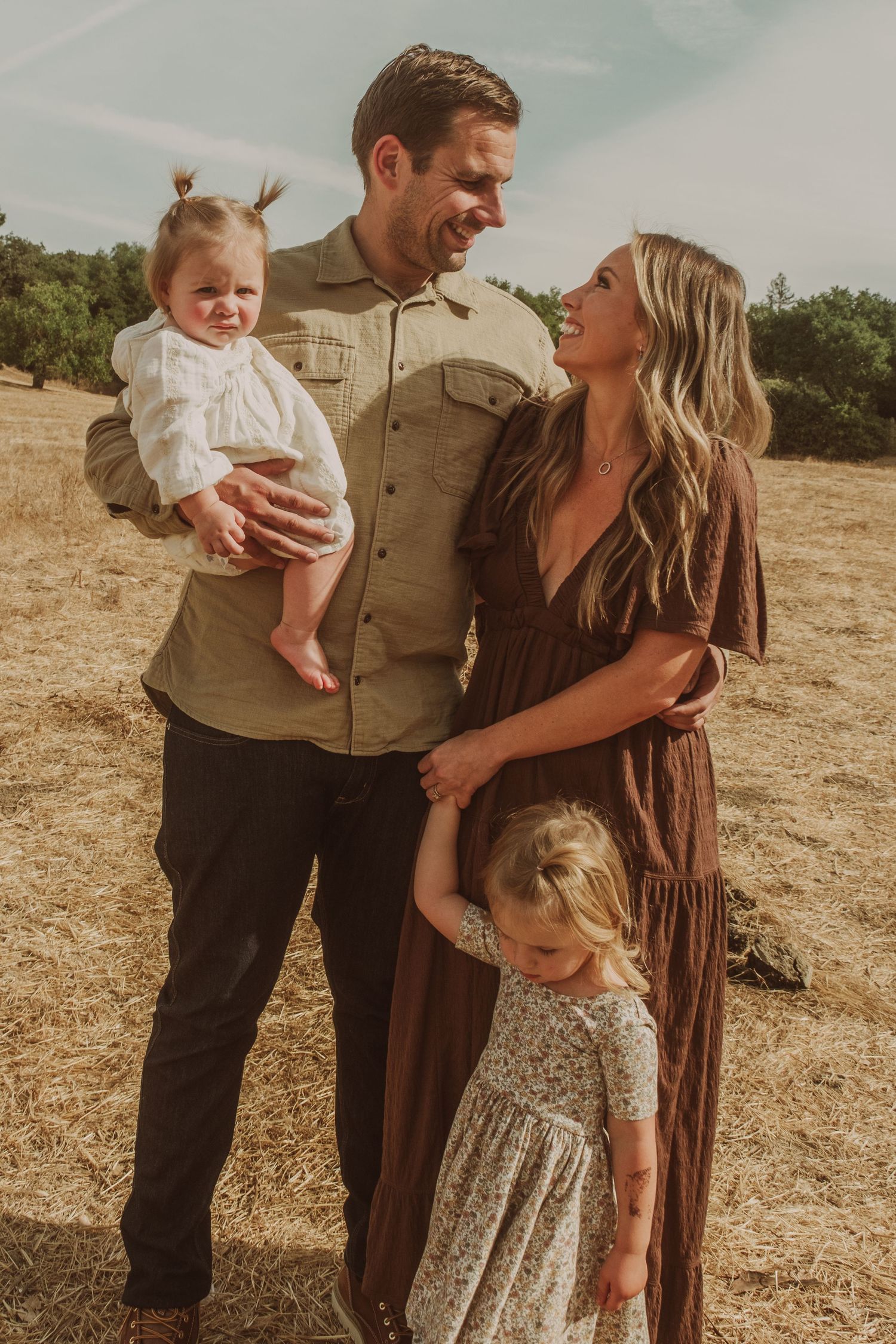 A family shares candid moments together in an outdoor setting with earth-toned clothing.