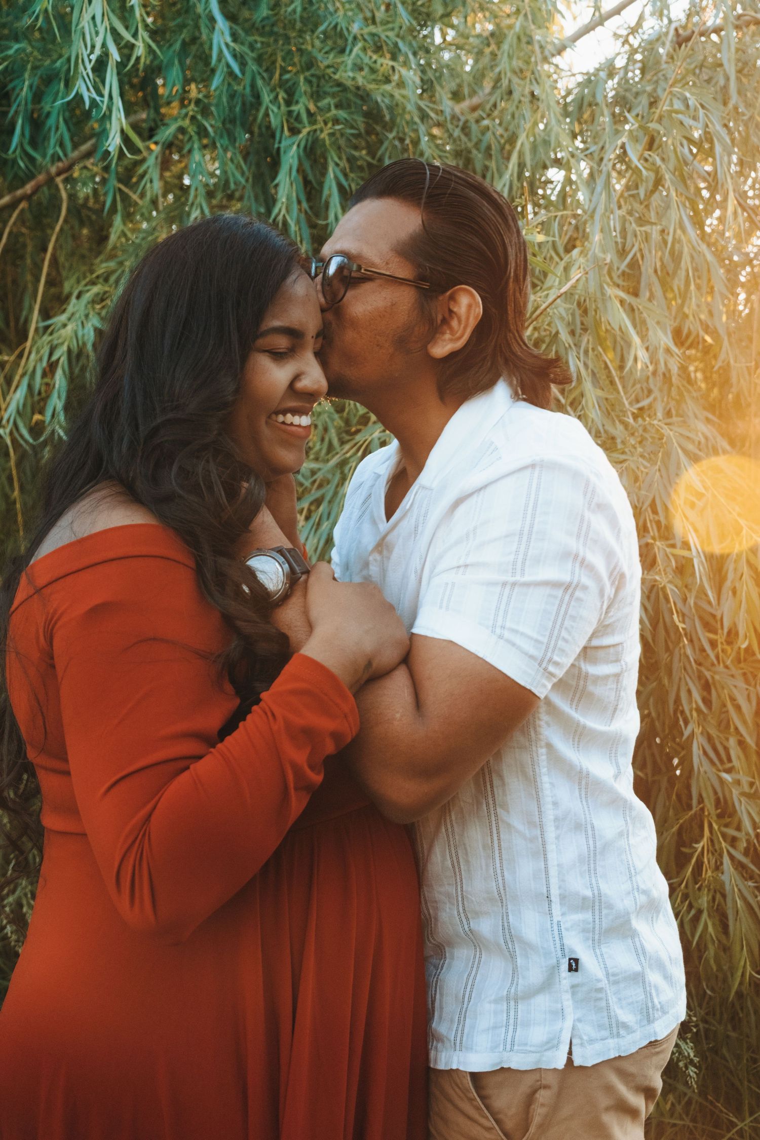 A romantic couple embracing in a sunlit garden with warm golden light filtering through trees.