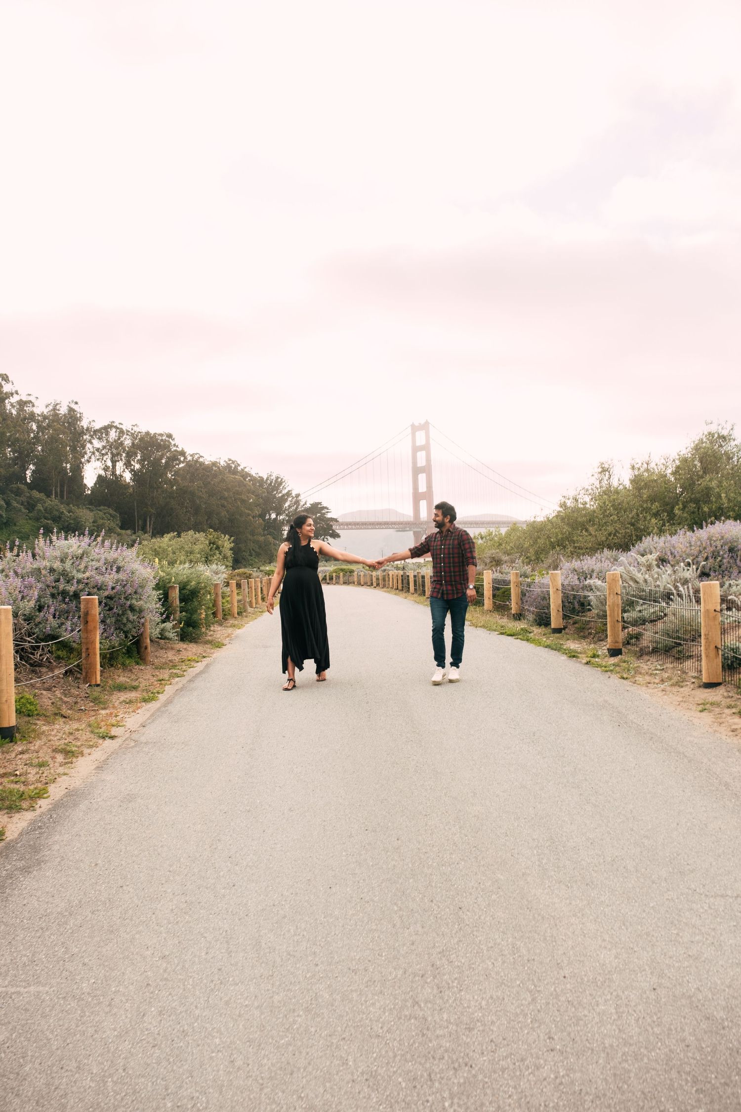 Couple walking on path near Golden Gate Bridge on foggy day.