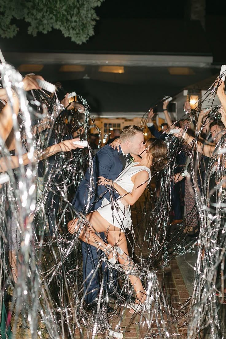 People celebrate and dance through a fountain spray at night during what appears to be an outdoor party or event.