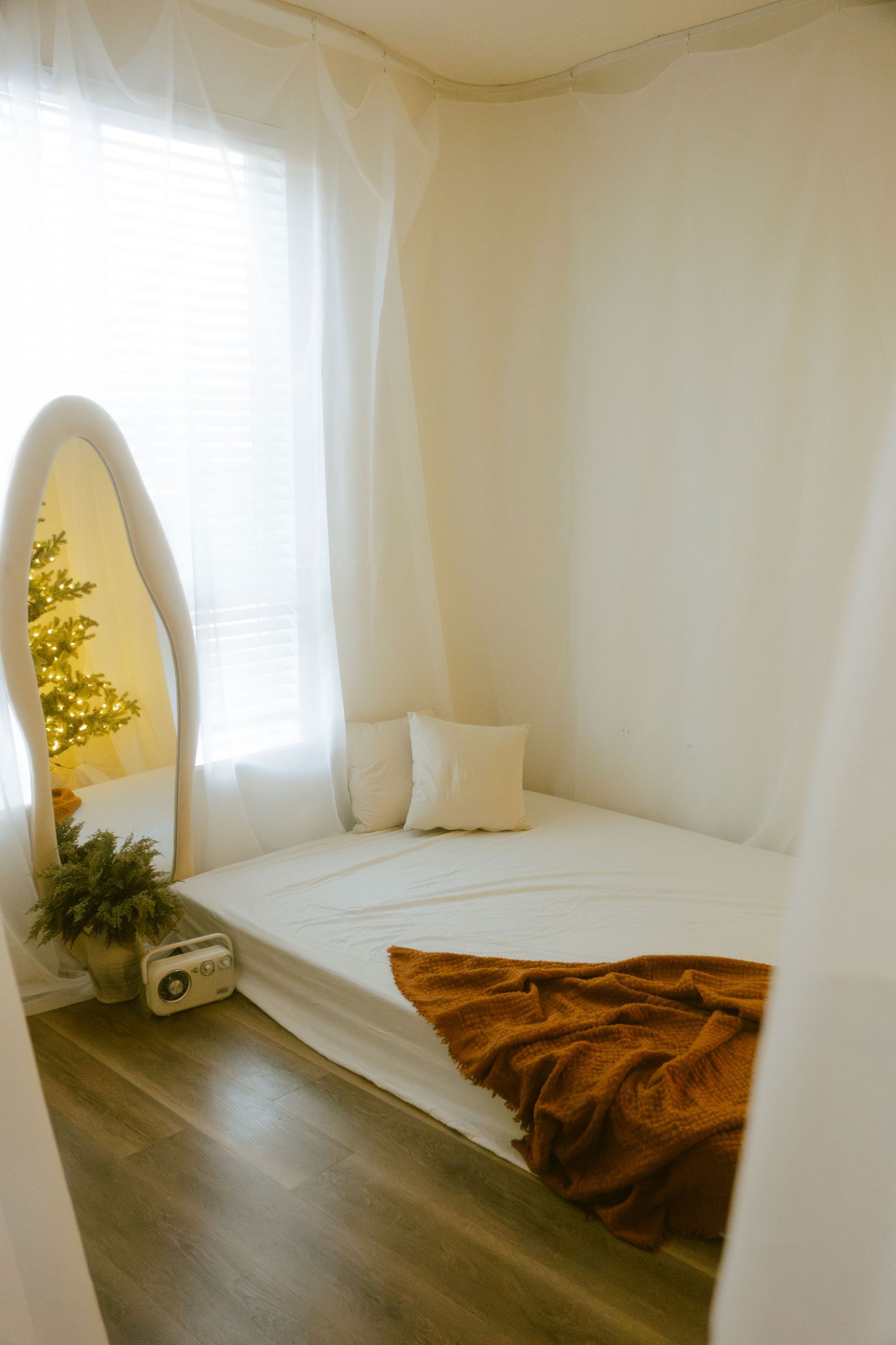 White room with arched mirror reflecting lit Christmas tree and brown throw blanket.