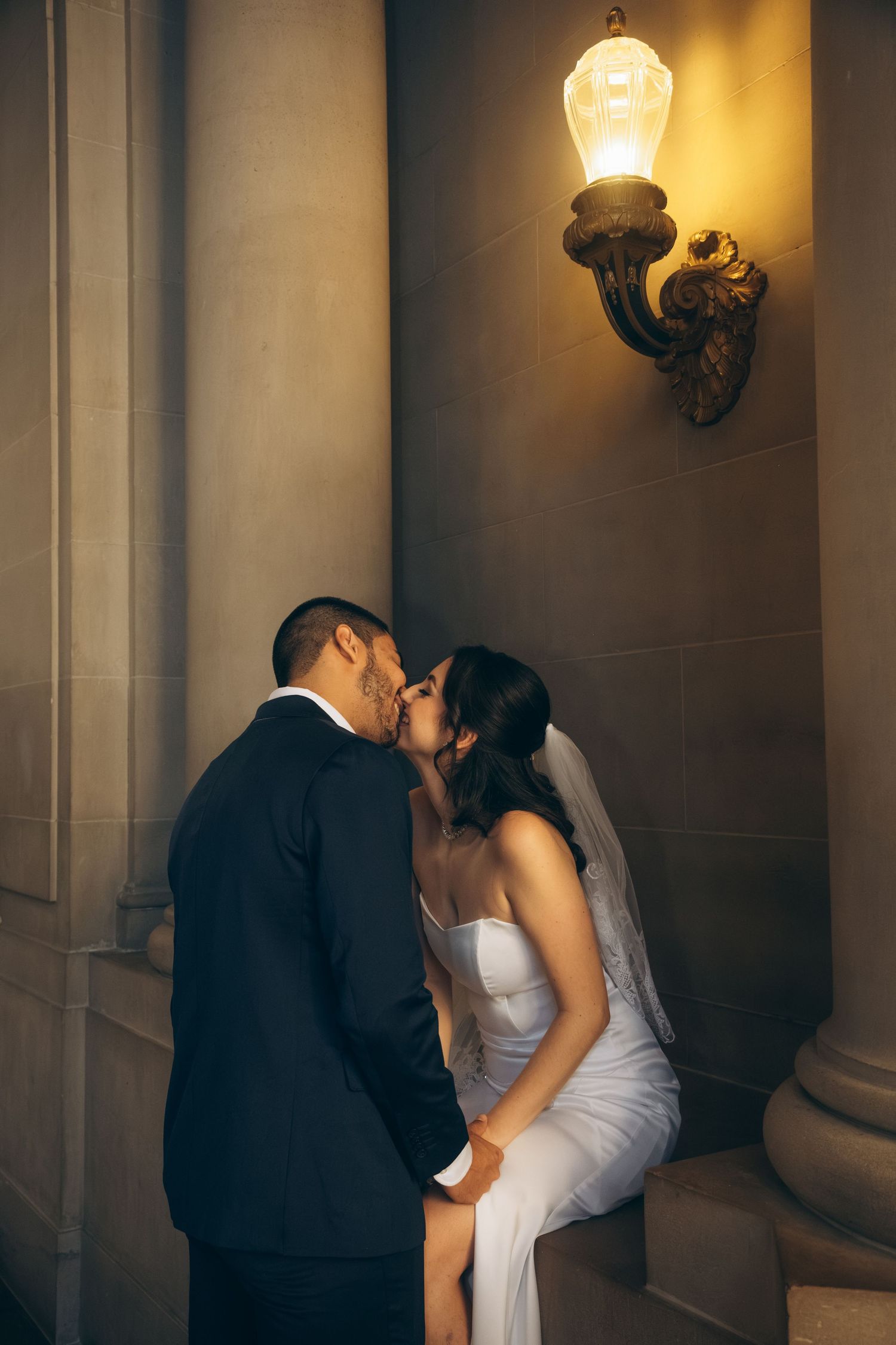 Intimate wedding portrait against a dark wall with ambient lighting.