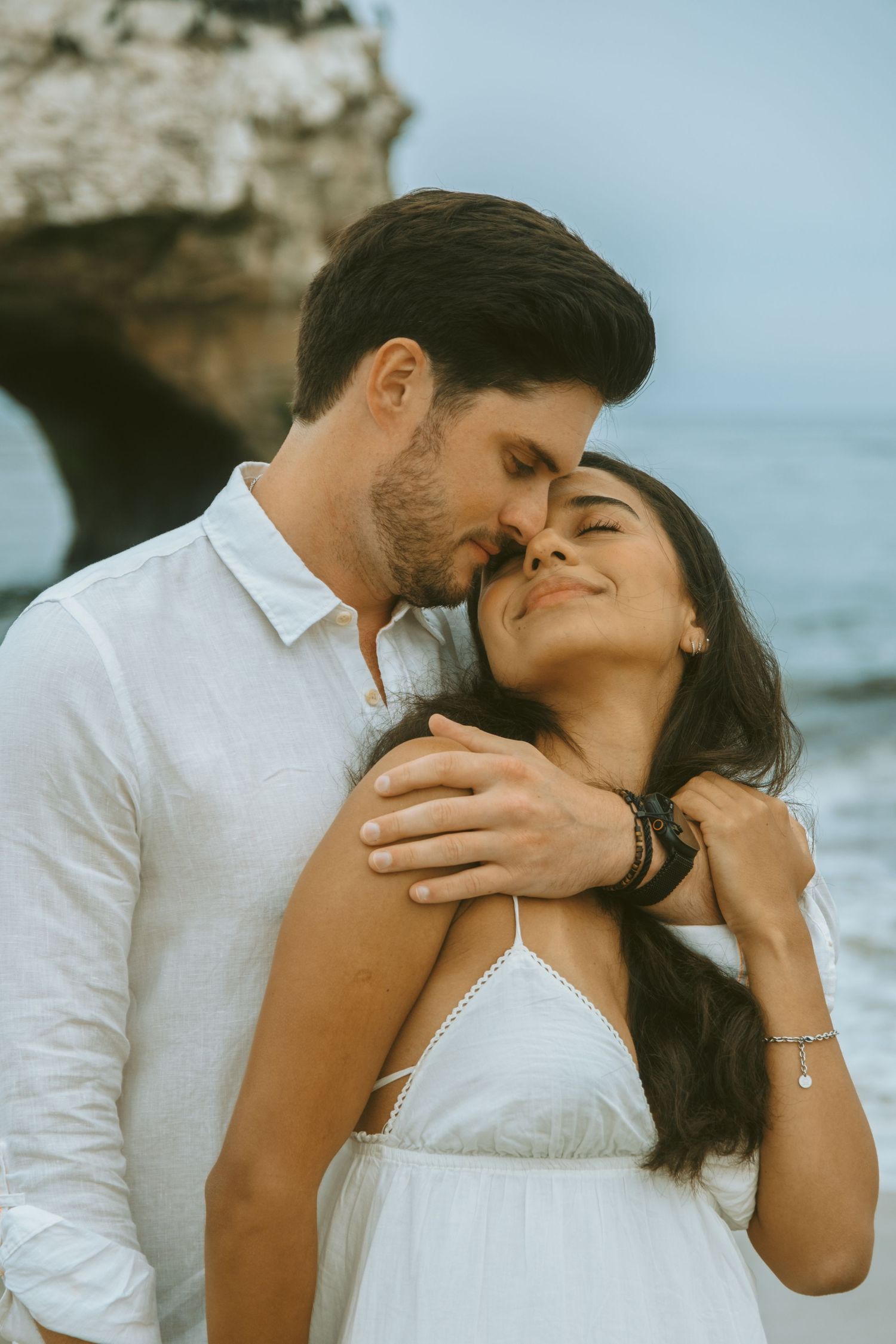 Romantic beach scene with couple in white clothing against ocean backdrop.