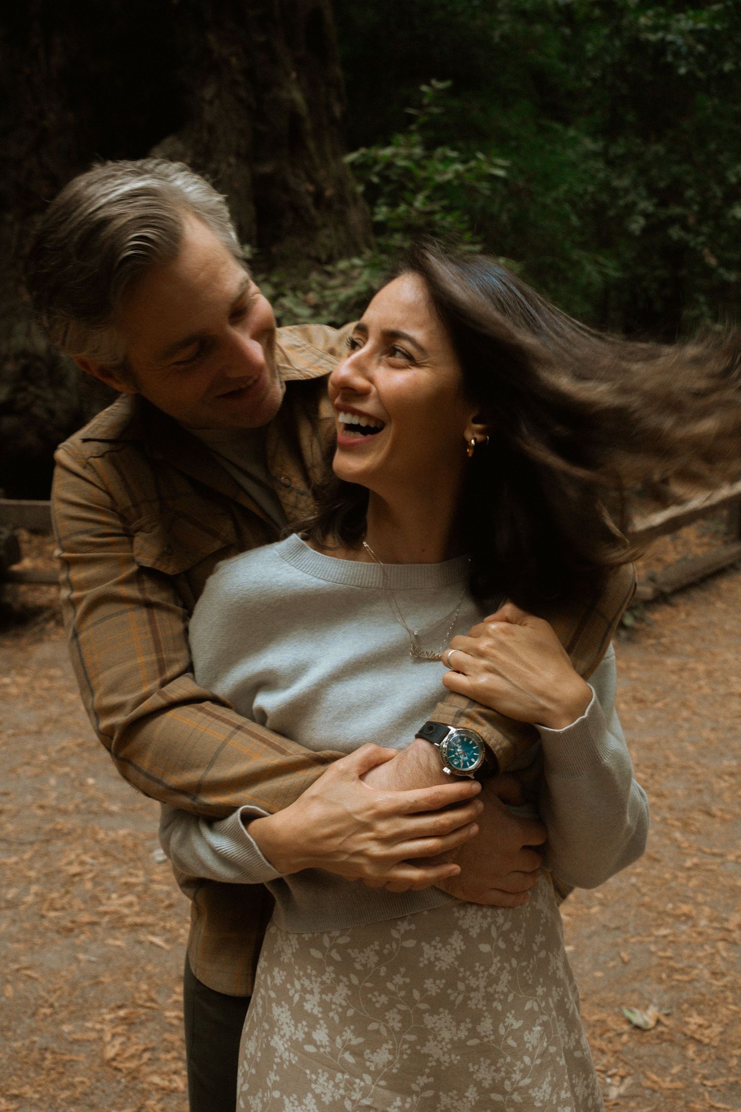 Candid moment of laughter and embrace in a forest setting with warm autumn tones.
