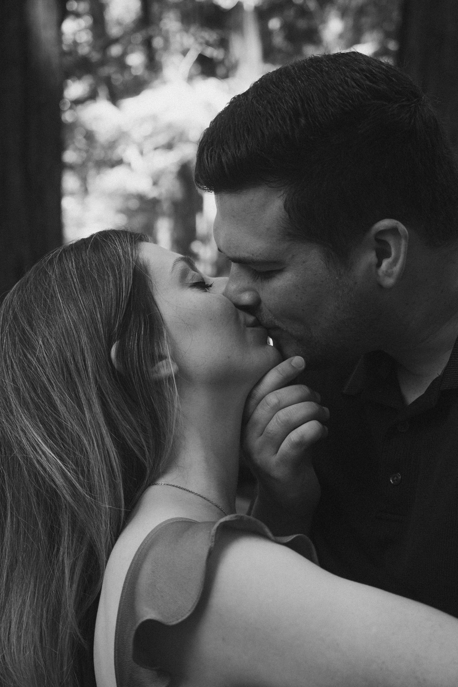 An intimate black and white portrait of a couple sharing a romantic moment in the woods.