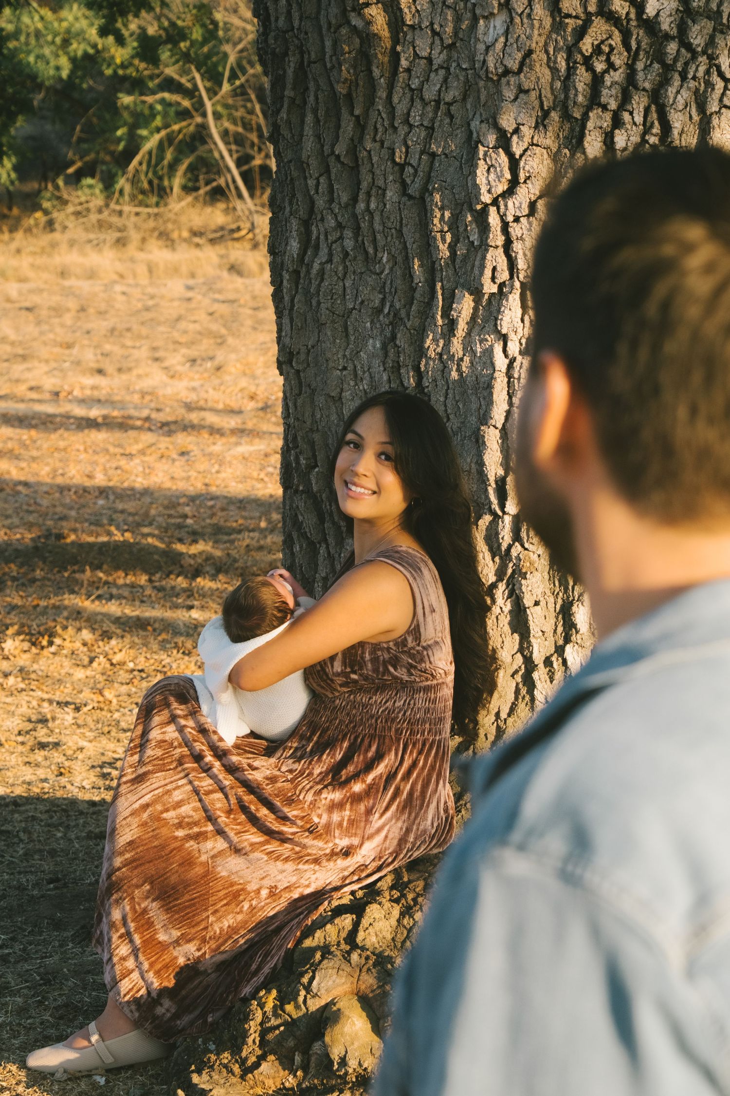 Romantic couple poses by a large tree trunk during golden hour photography session.