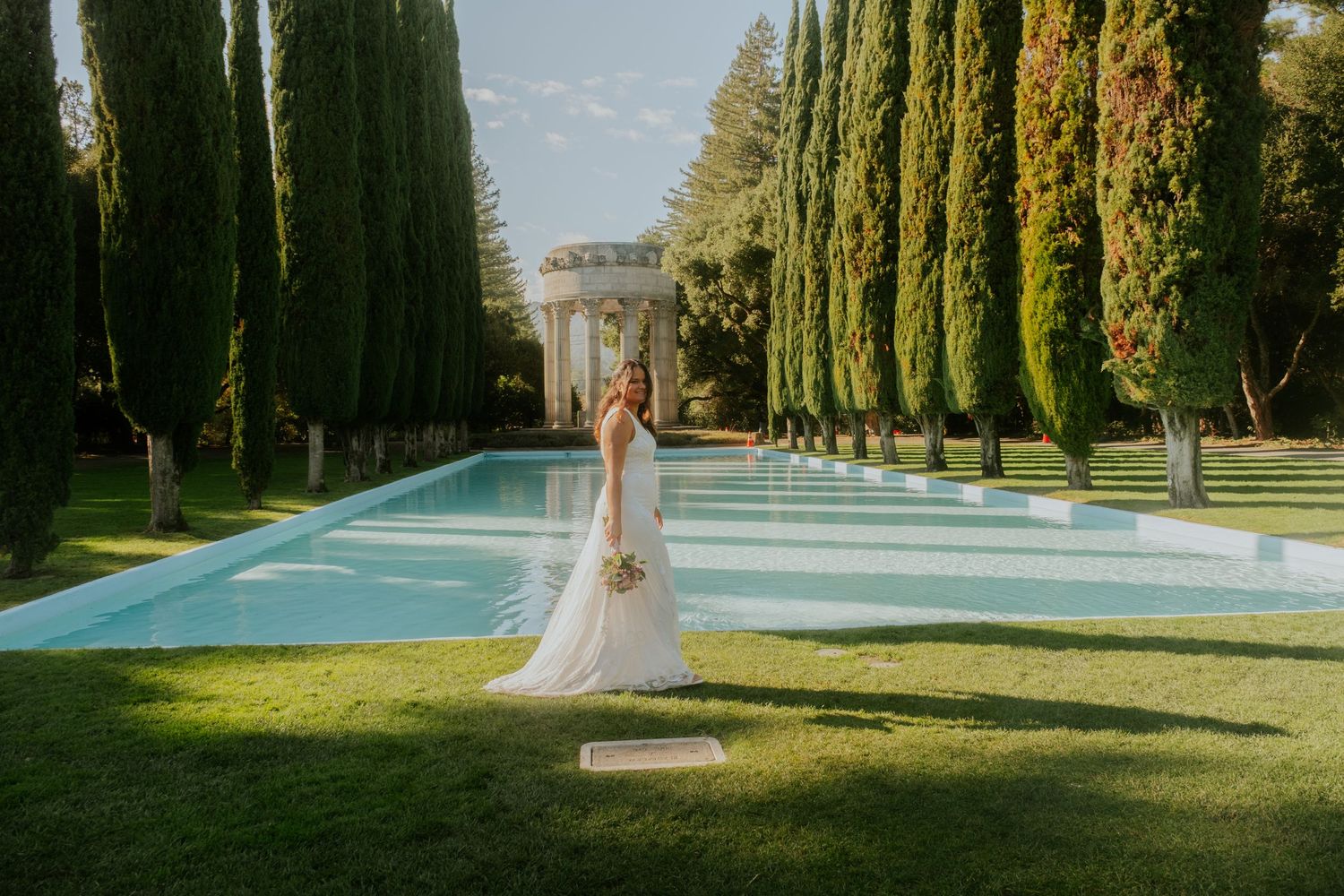 Wedding venue with elegant cypress trees lining a path beside a swimming pool.