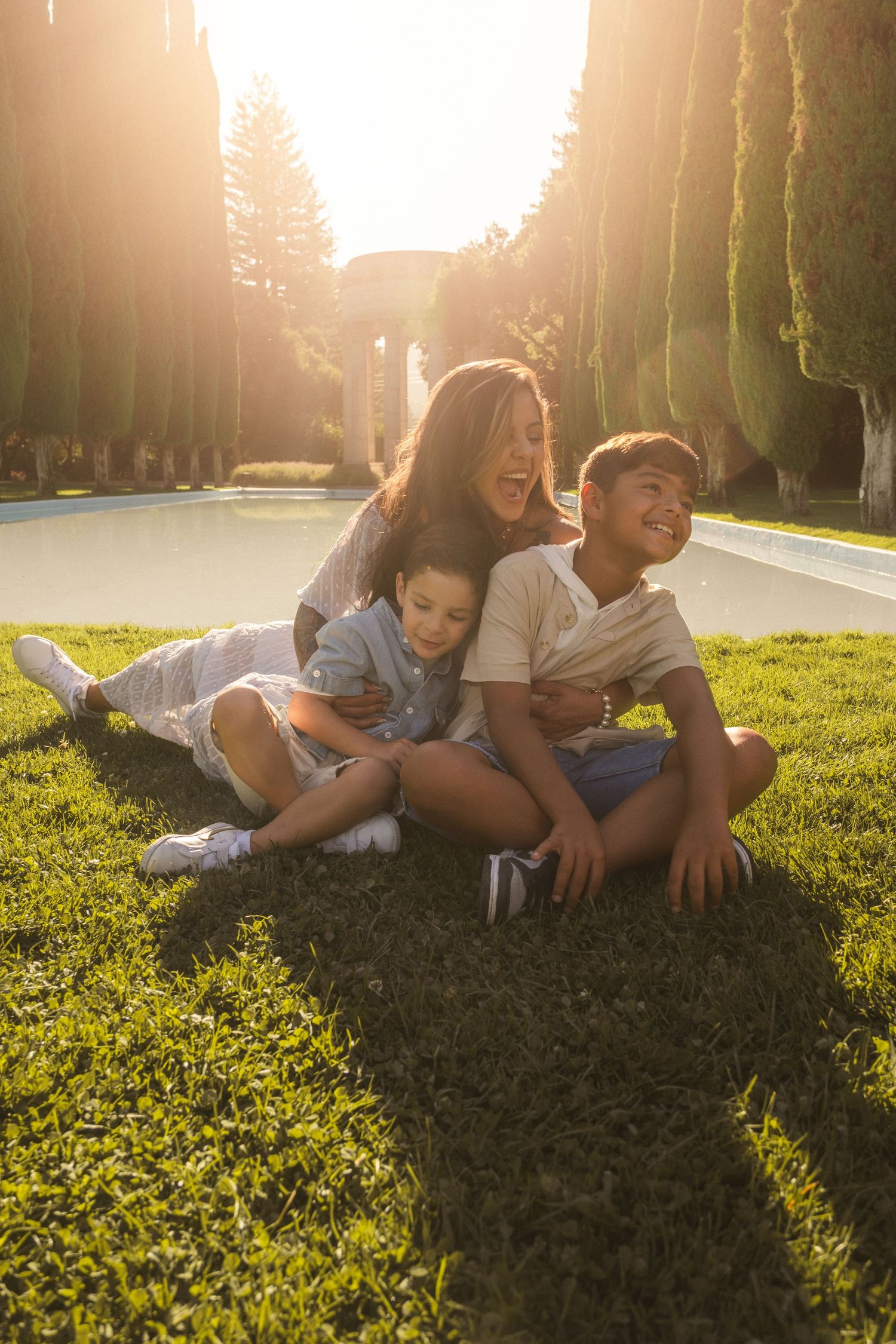 Family relaxing together on sunny grass lawn during golden hour sunset.