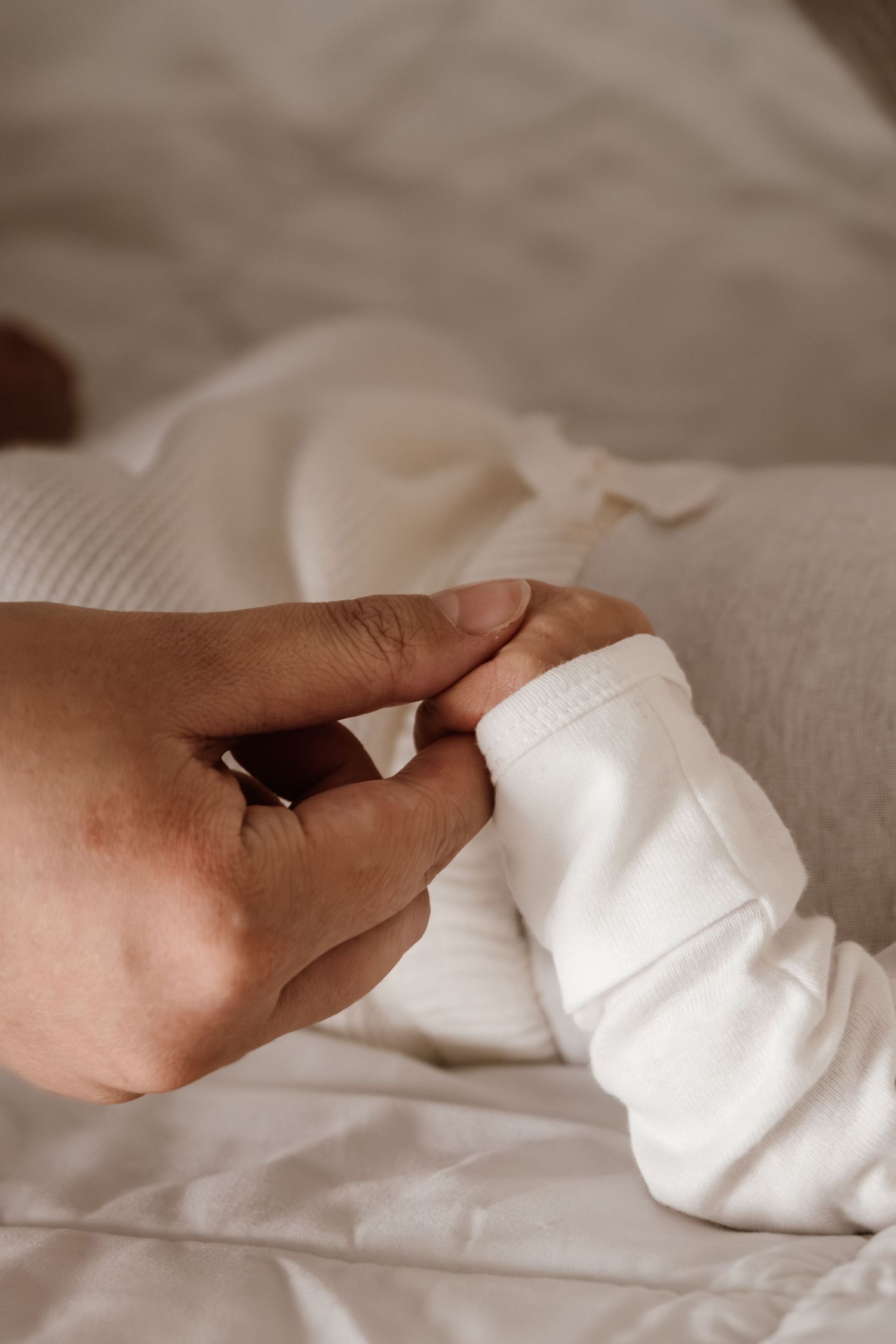 A sequence of hands gently folding white bedsheets or linens in a soft, neutral setting.