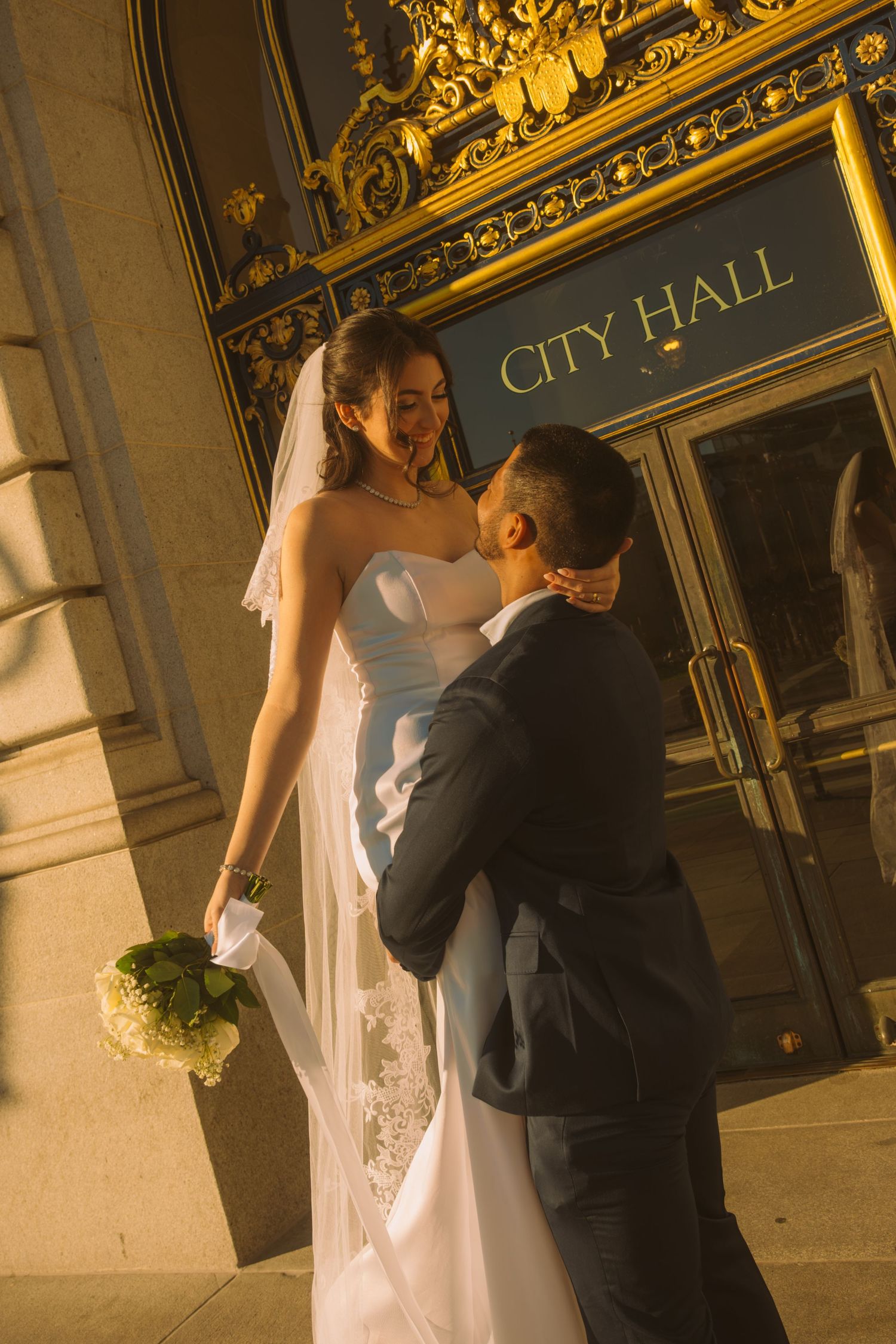 Romantic moment captured outside historic City Hall entrance at golden hour.
