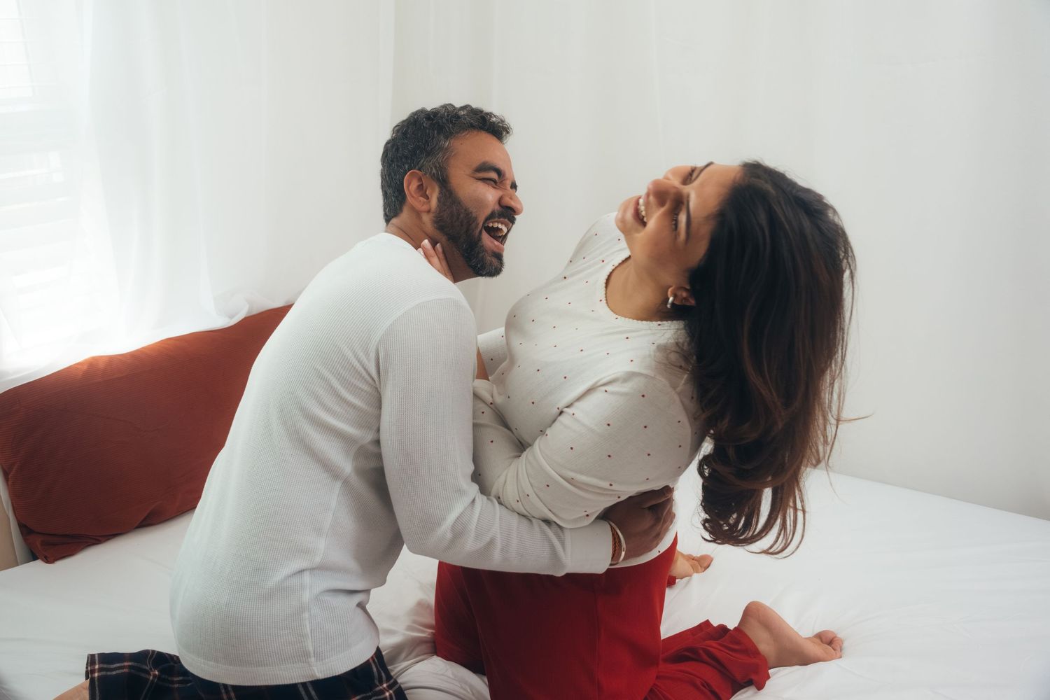 Couple in white and red clothing embracing in bright living room.