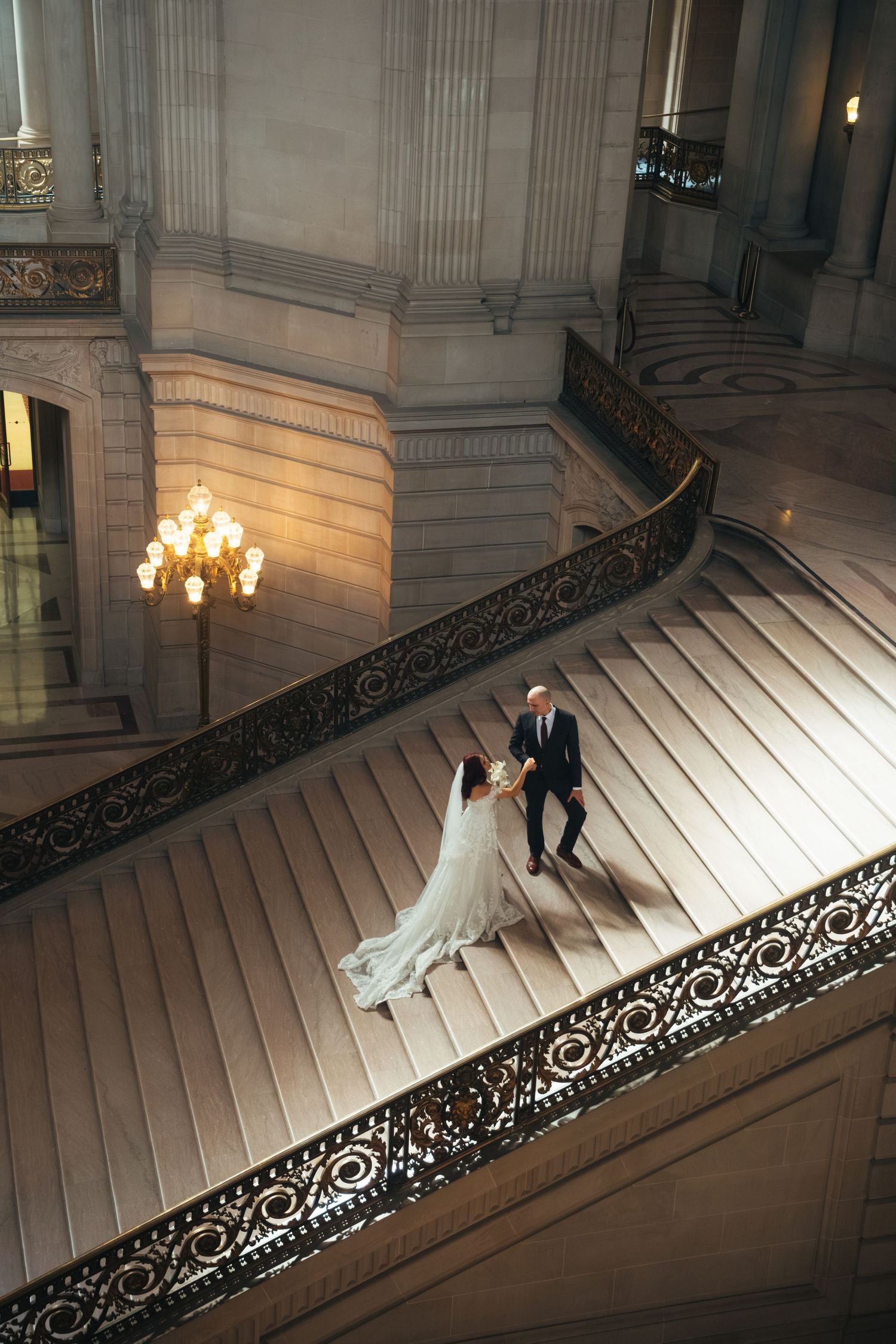 A couple descends an elegant grand staircase in dramatic lighting.