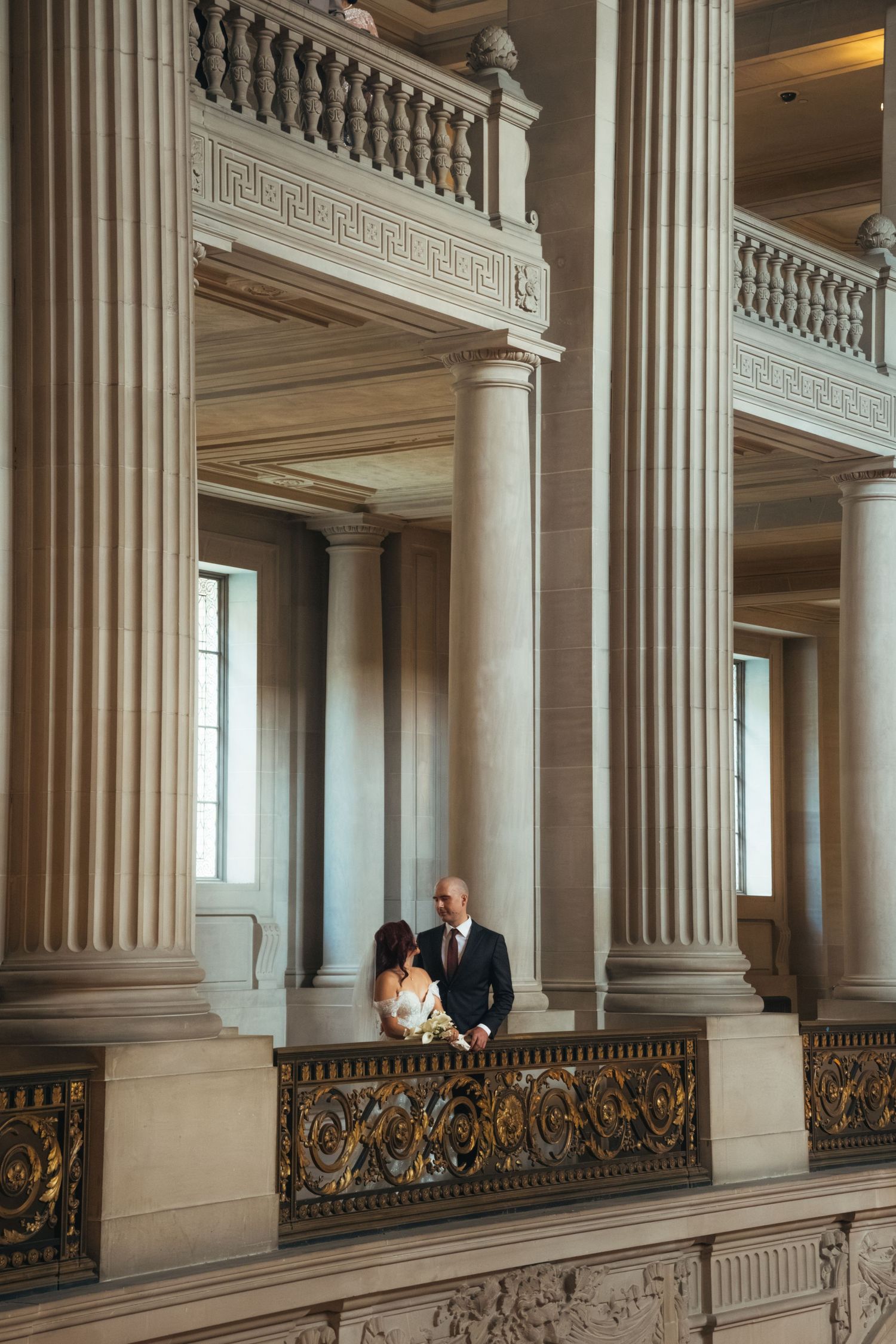 Wedding couple poses between grand marble columns in an elegant historic building.