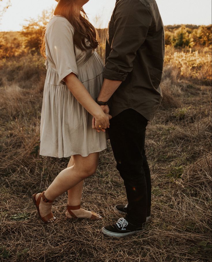 Romantic couple holding hands in casual attire during golden hour photoshoot in field.