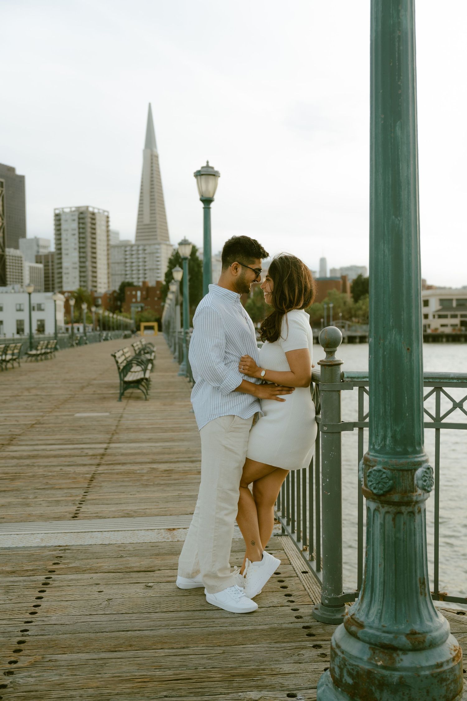 Couple embracing on San Francisco pier with Transamerica Pyramid in background.