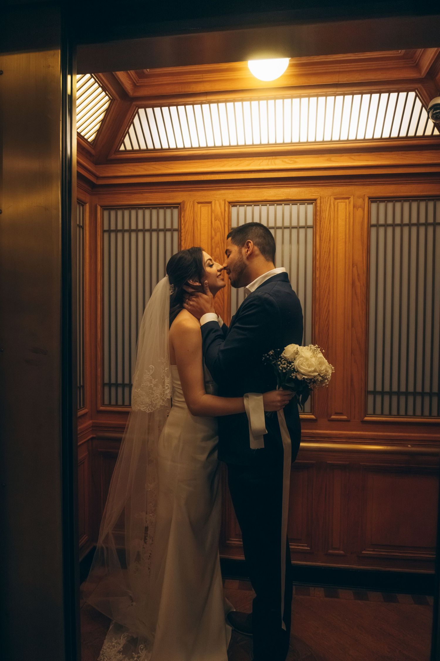 Wedding couple embracing in a warmly lit wooden-paneled corridor.