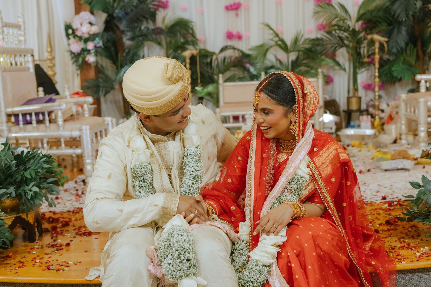 Indian bride in red saree and groom in white sherwani exchange garlands at traditional Hindu wedding ceremony.