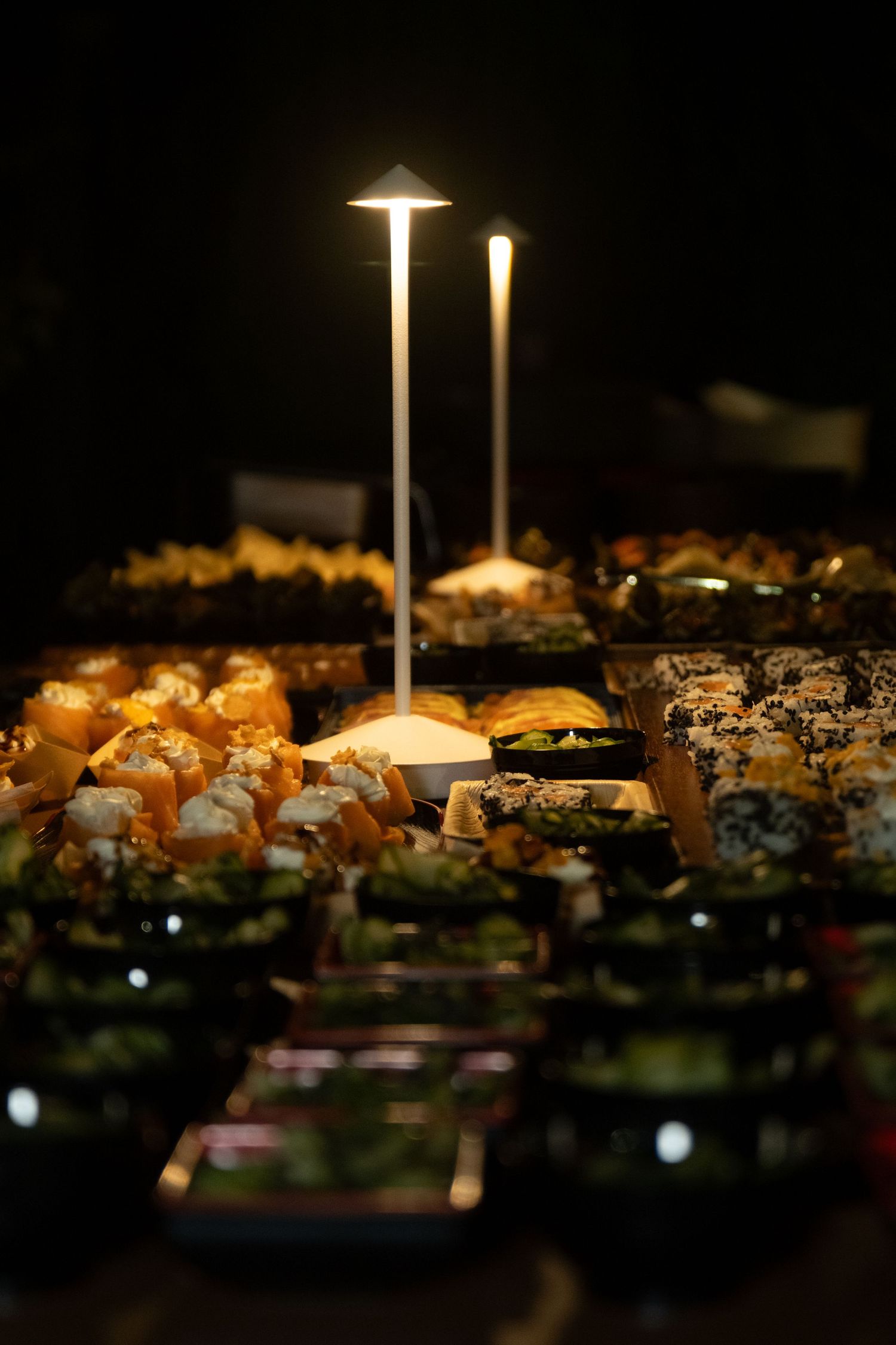 Elegant sushi buffet display illuminated by tall slim candle lamps in a dark ambient restaurant setting.