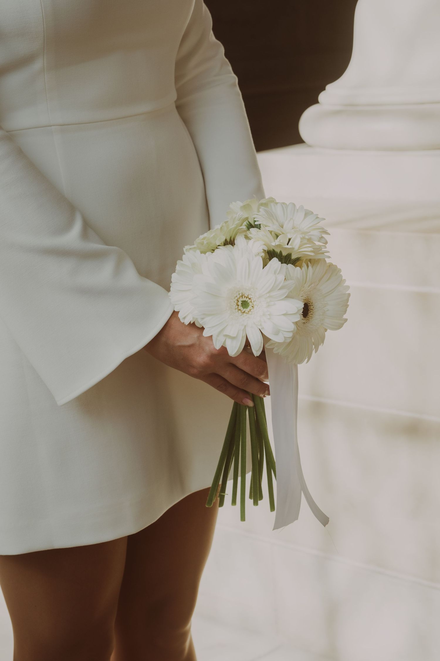 Elegant white gerbera daisy bouquet against a white wedding dress.