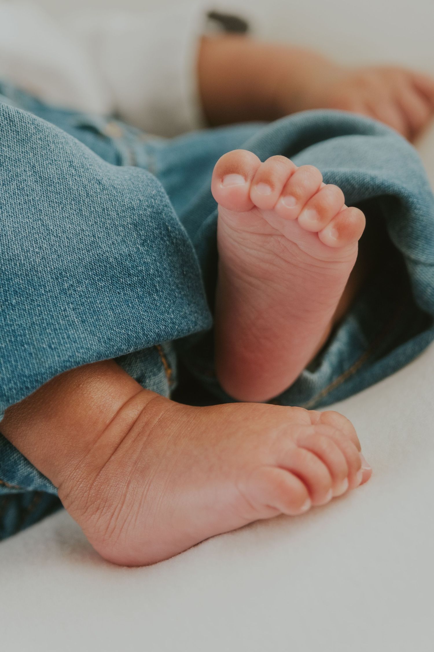 Tiny infant feet with delicate toes resting on teal blue fabric.