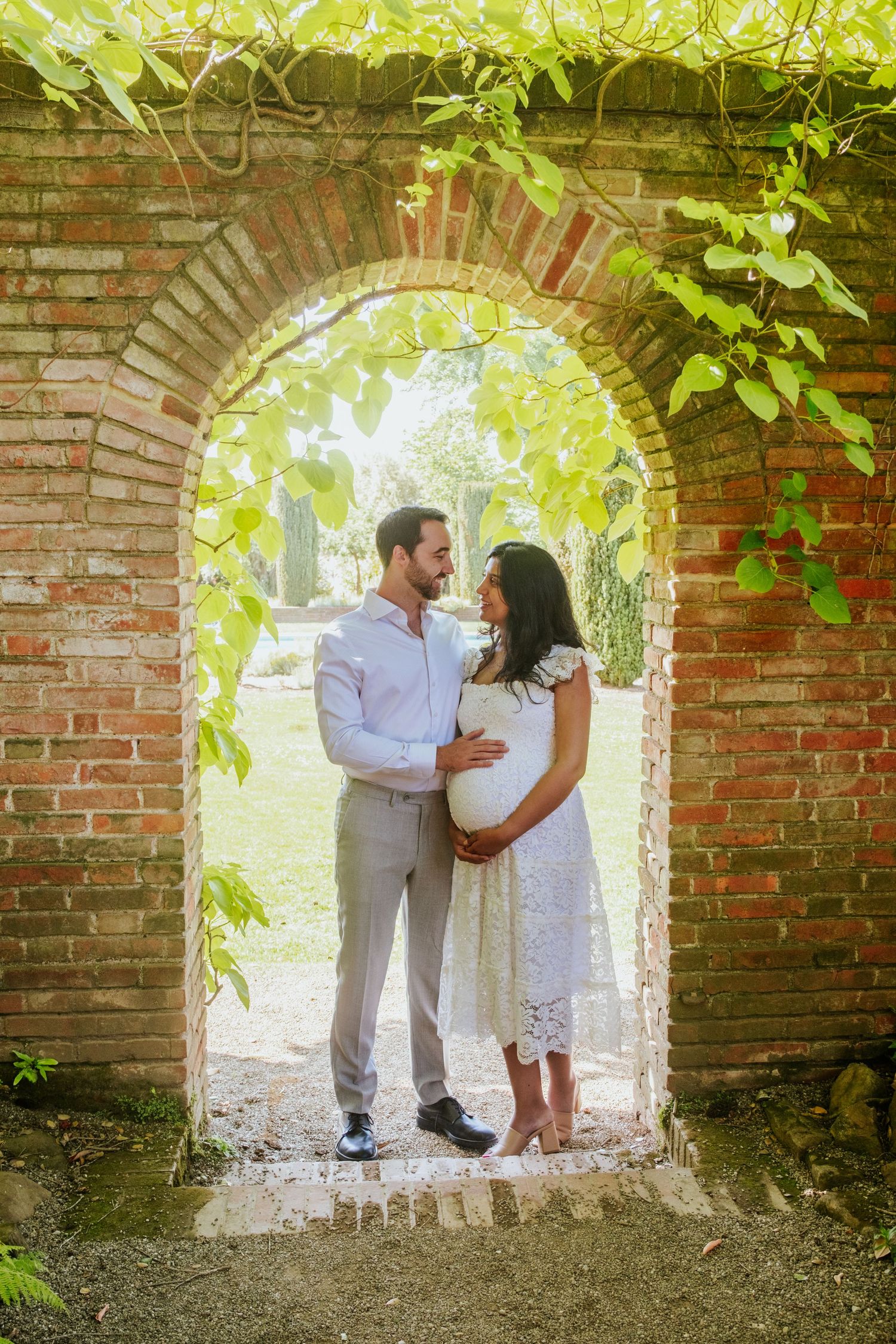 Couple sharing romantic moment through brick garden archway with green vines.