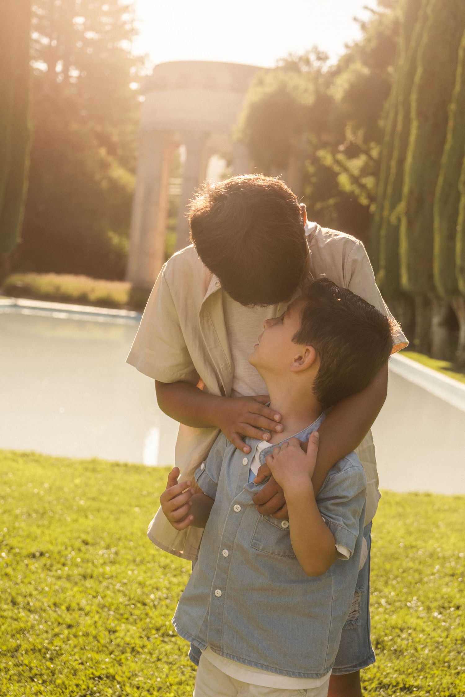 A tender moment captured in warm sunlight with cypress trees in the background.