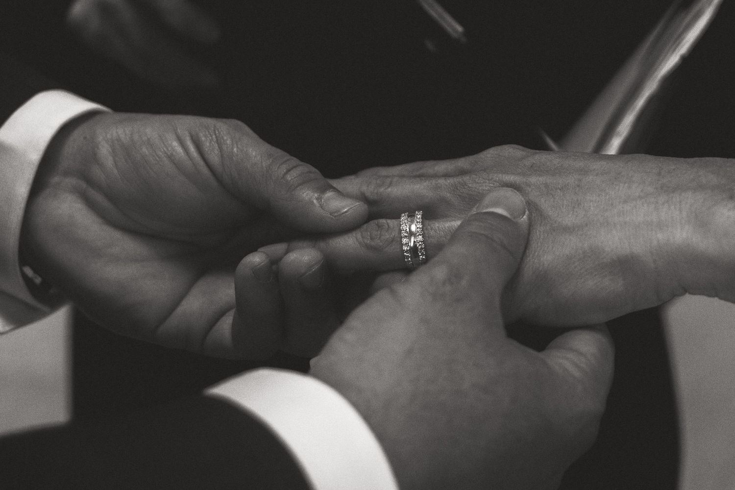 Close-up shots of hands exchanging wedding rings in dramatic black and white.