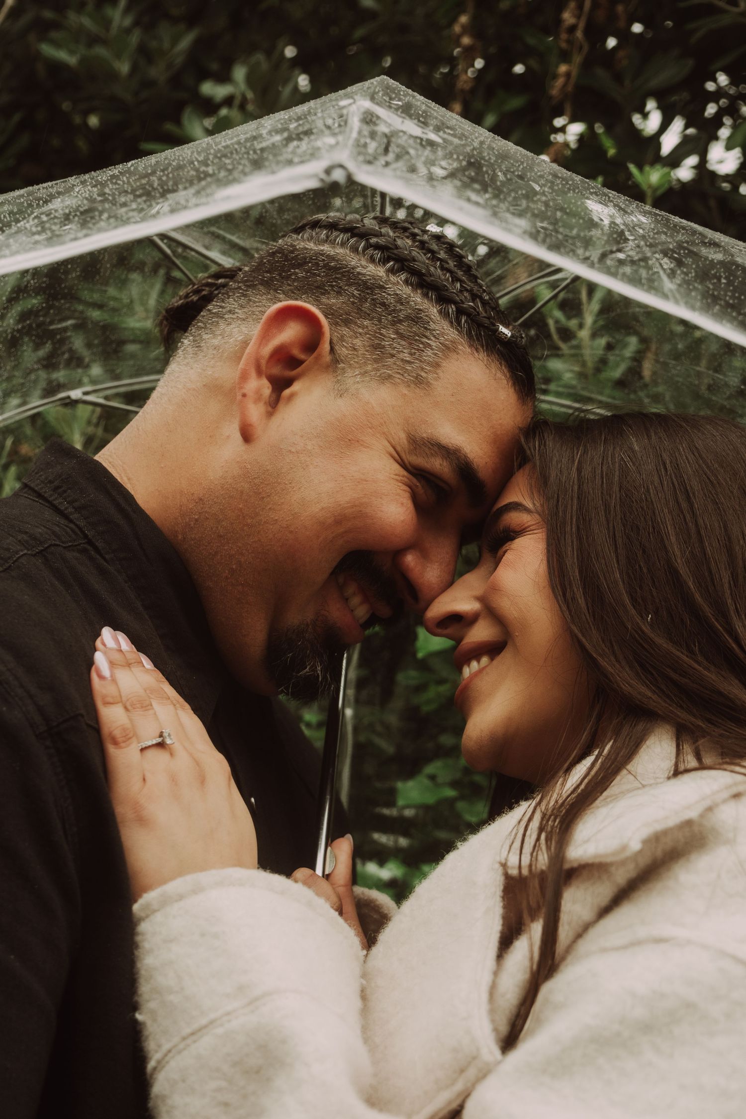 Romantic couple sharing tender moment under umbrella in natural outdoor setting.