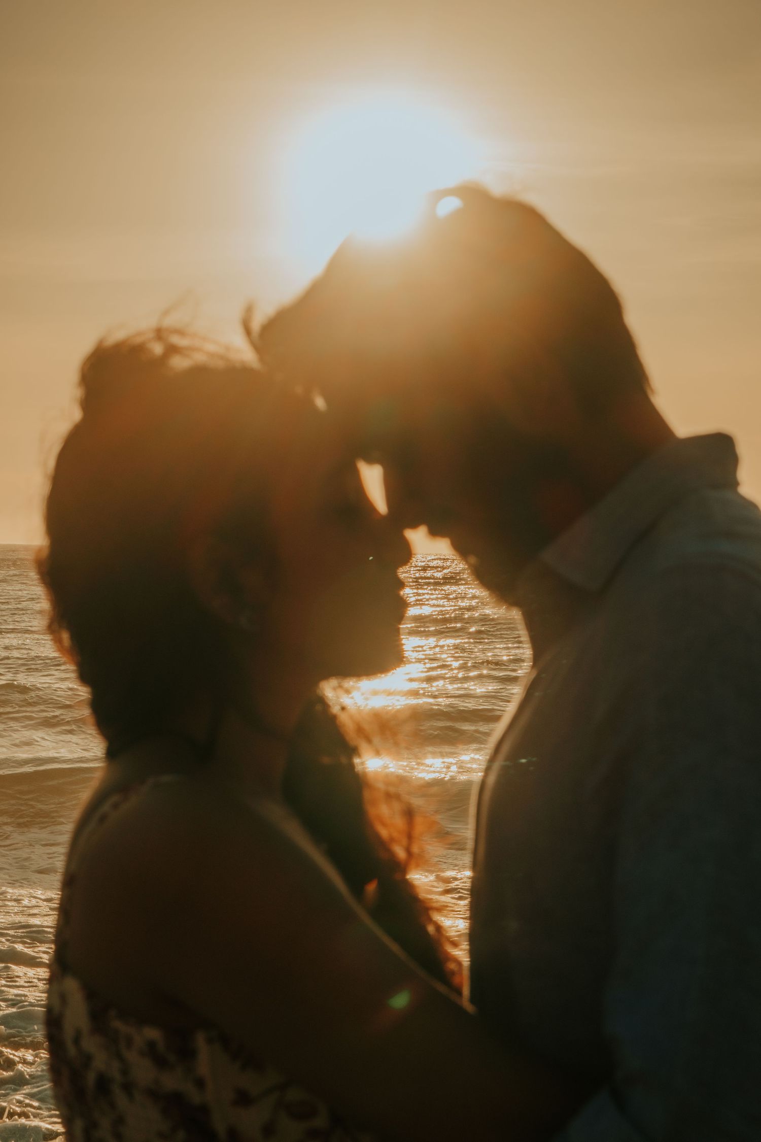 A silhouetted couple shares an intimate moment against a golden sunset on the beach.