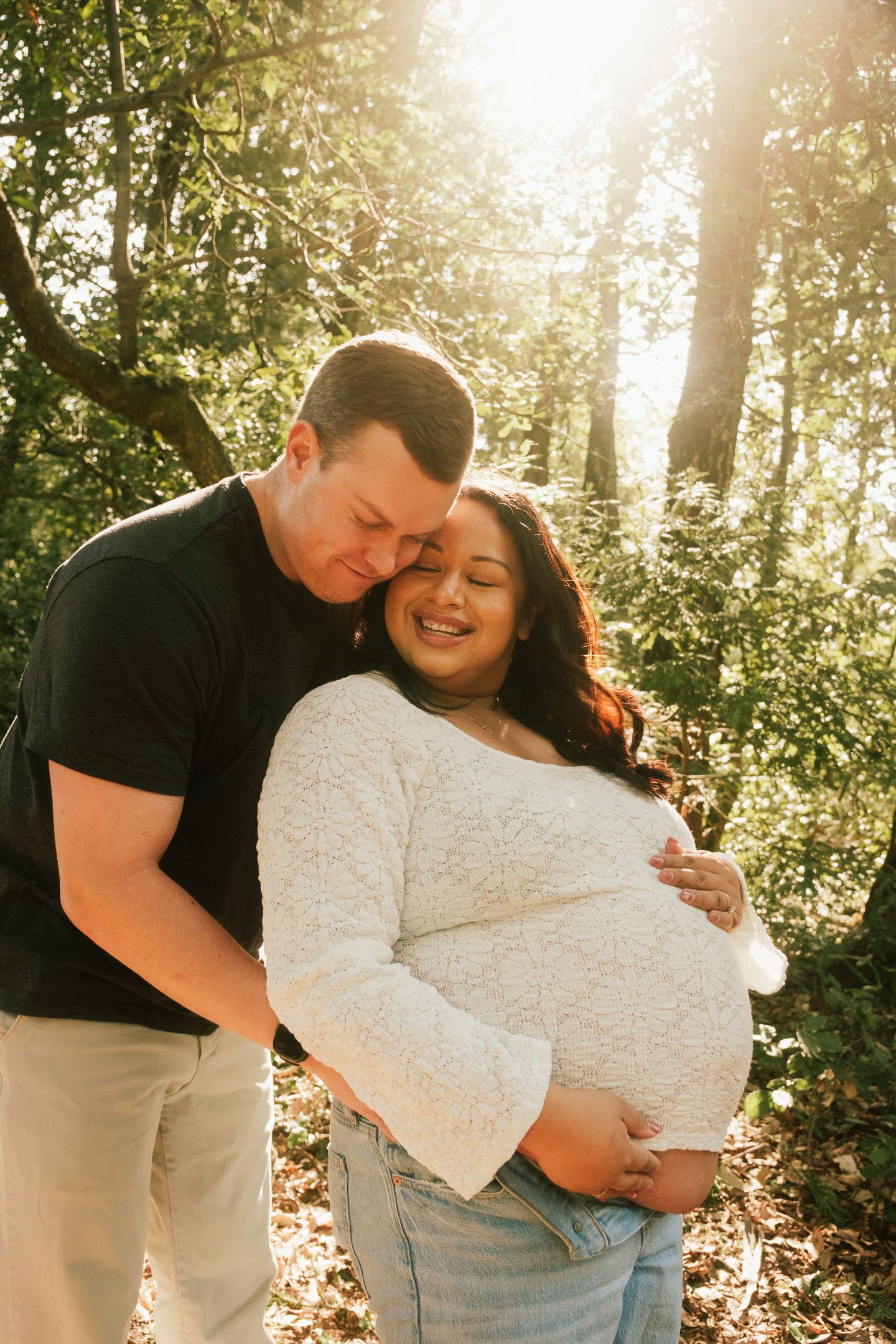 Couple embracing in a sunlit forest clearing during golden hour.