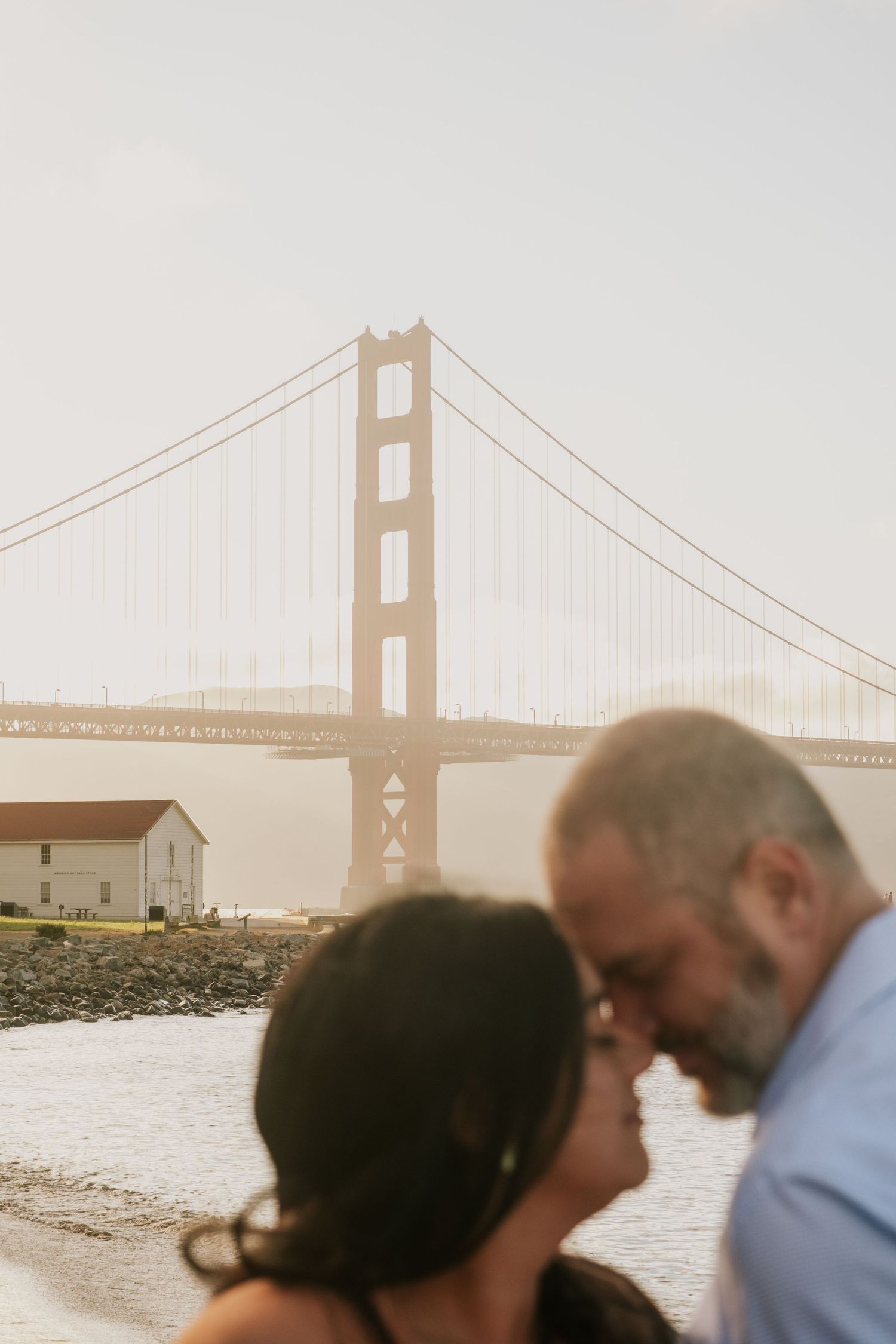Romantic couple embracing near Golden Gate Bridge during golden hour.
