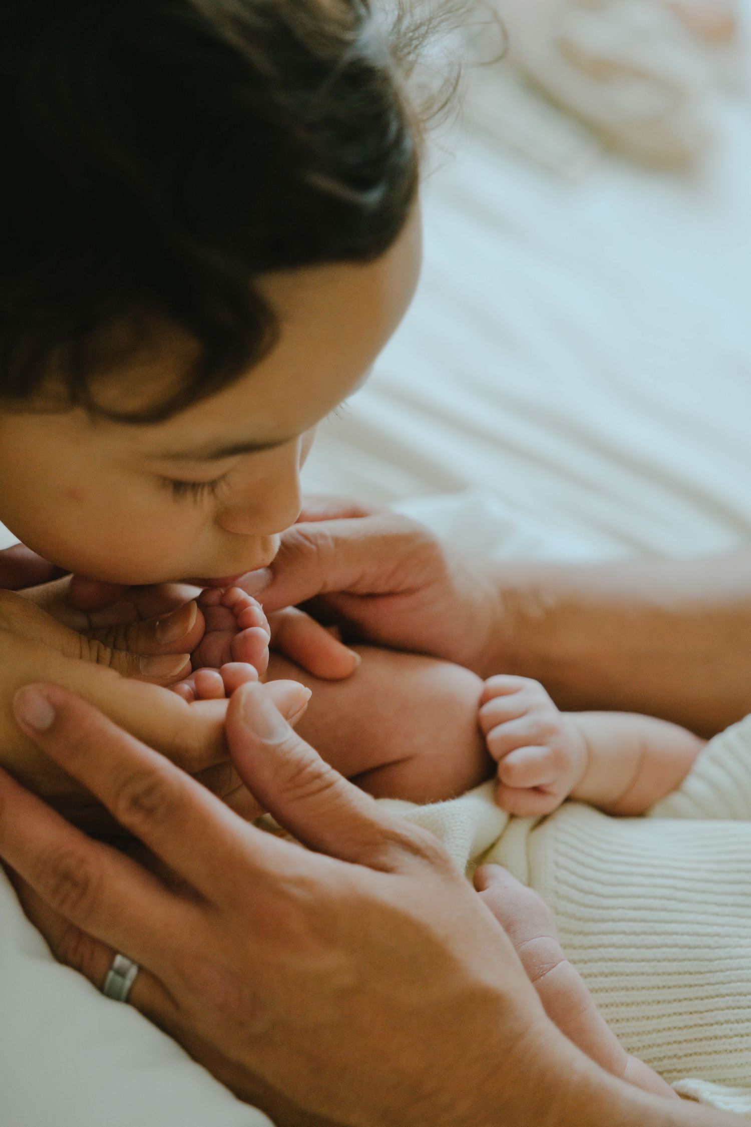 A tender moment as a mother kisses her newborn baby's tiny feet while a father's hands gently support them.