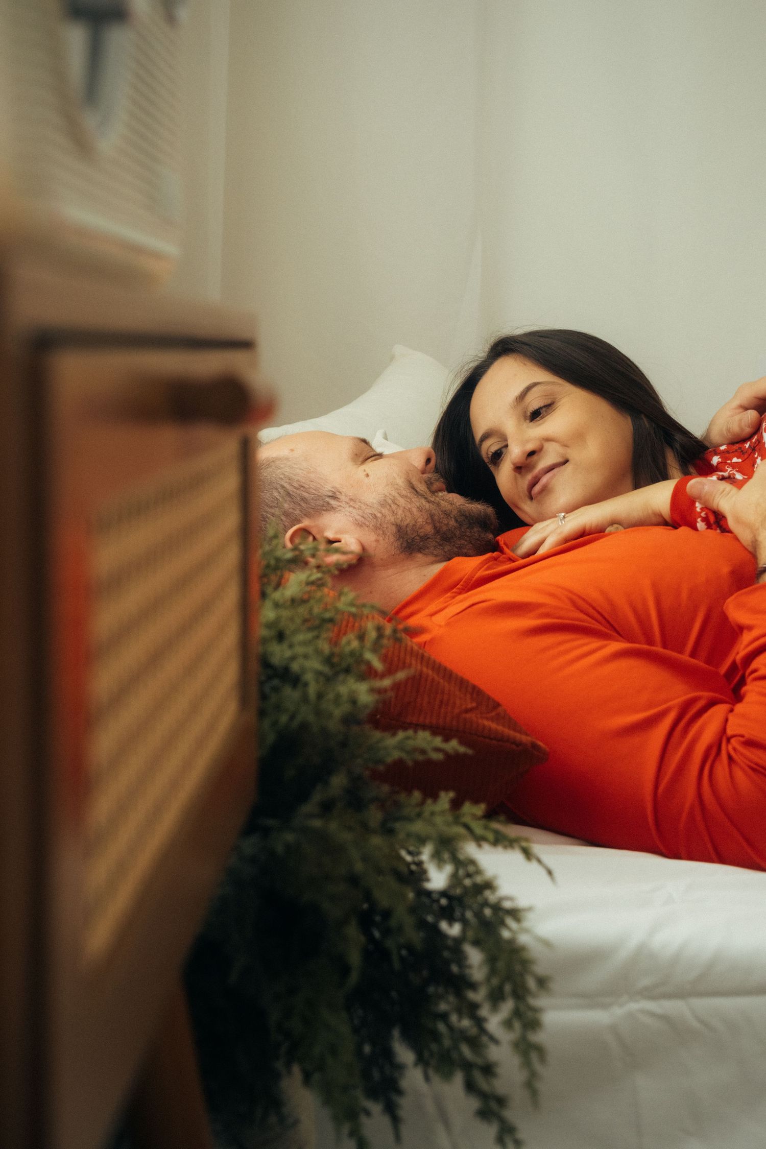 A couple sharing a peaceful moment while resting on white bedding with holiday decorations.