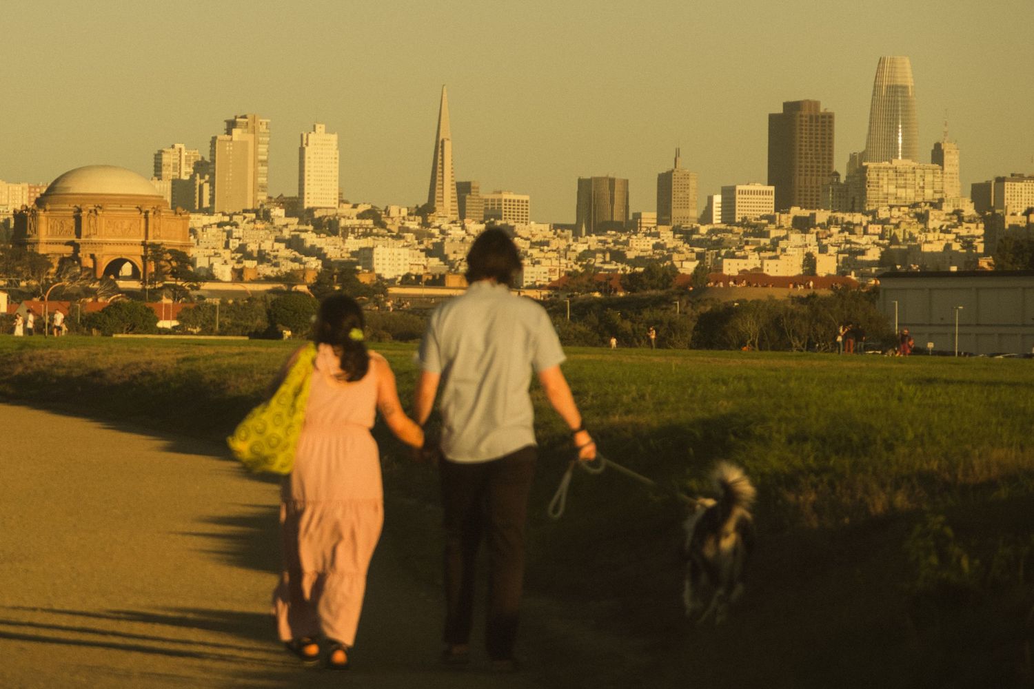 Couple walking along a hilltop path with San Francisco skyline in golden afternoon light.