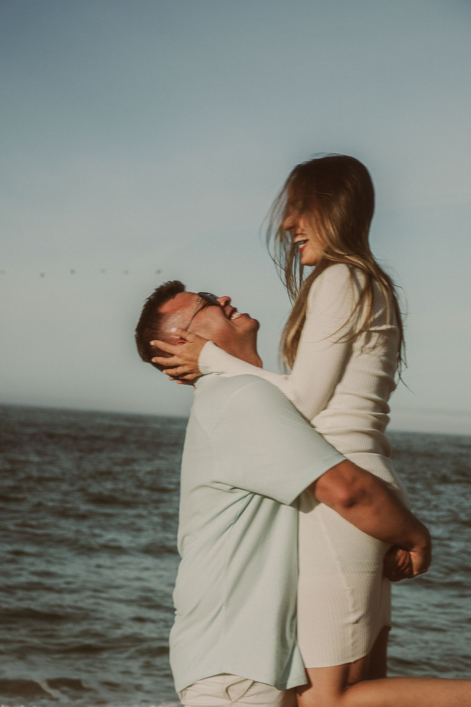 Romantic couple embracing on a beach at sunset with waves in the background.