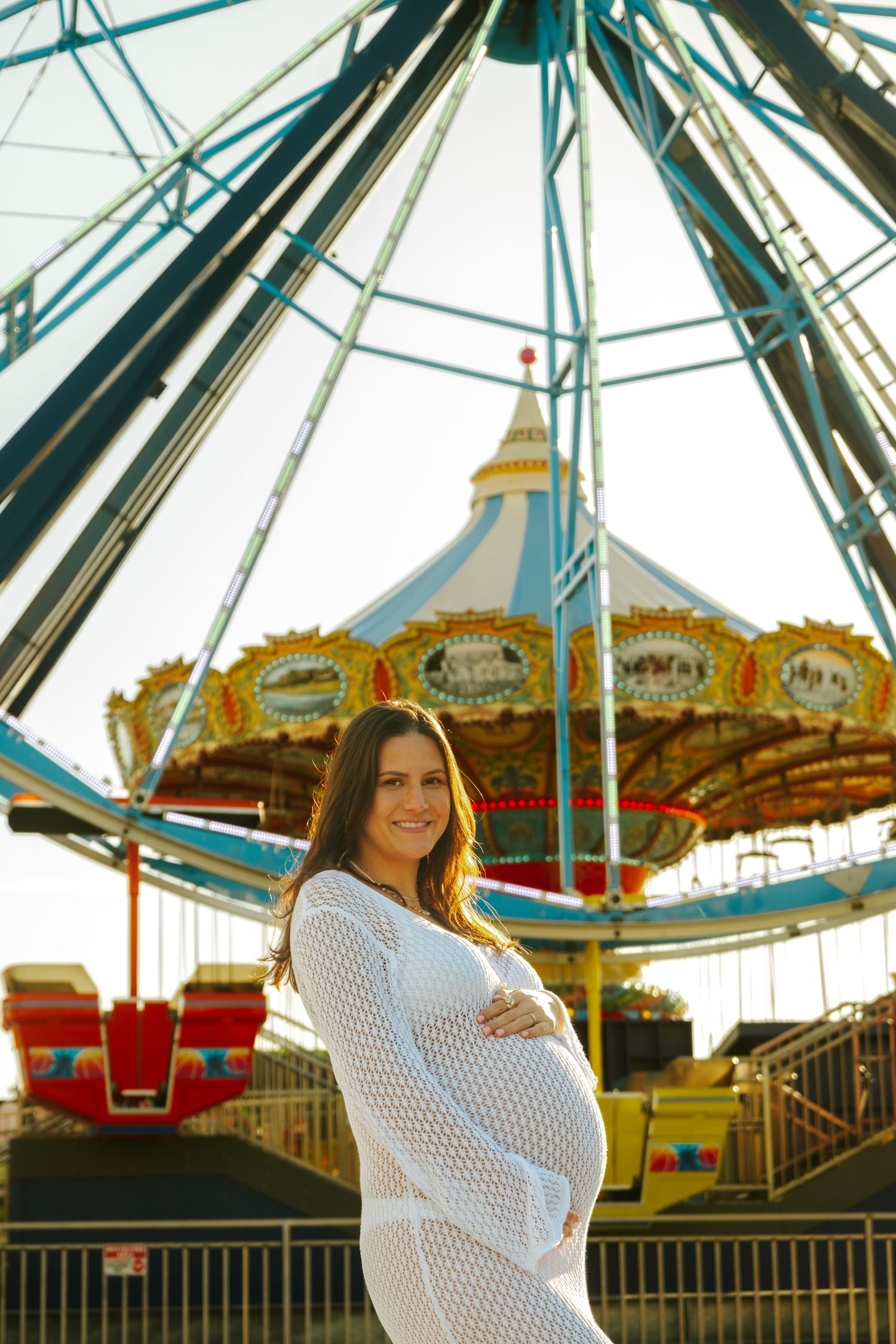 A woman in white poses confidently against carnival rides and attractions at sunset.