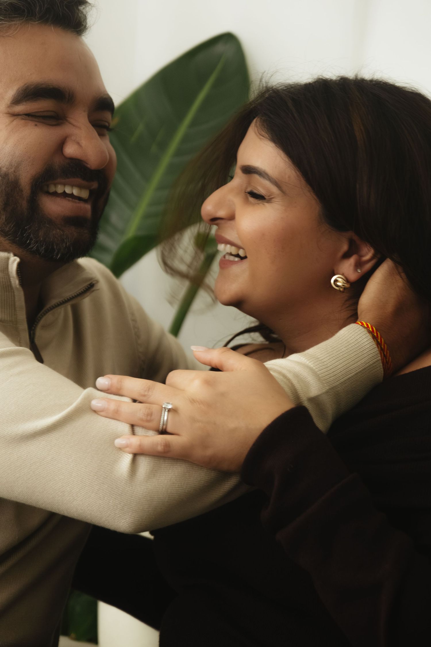 A joyful moment captured during a pregnancy photoshoot with green plants in background.