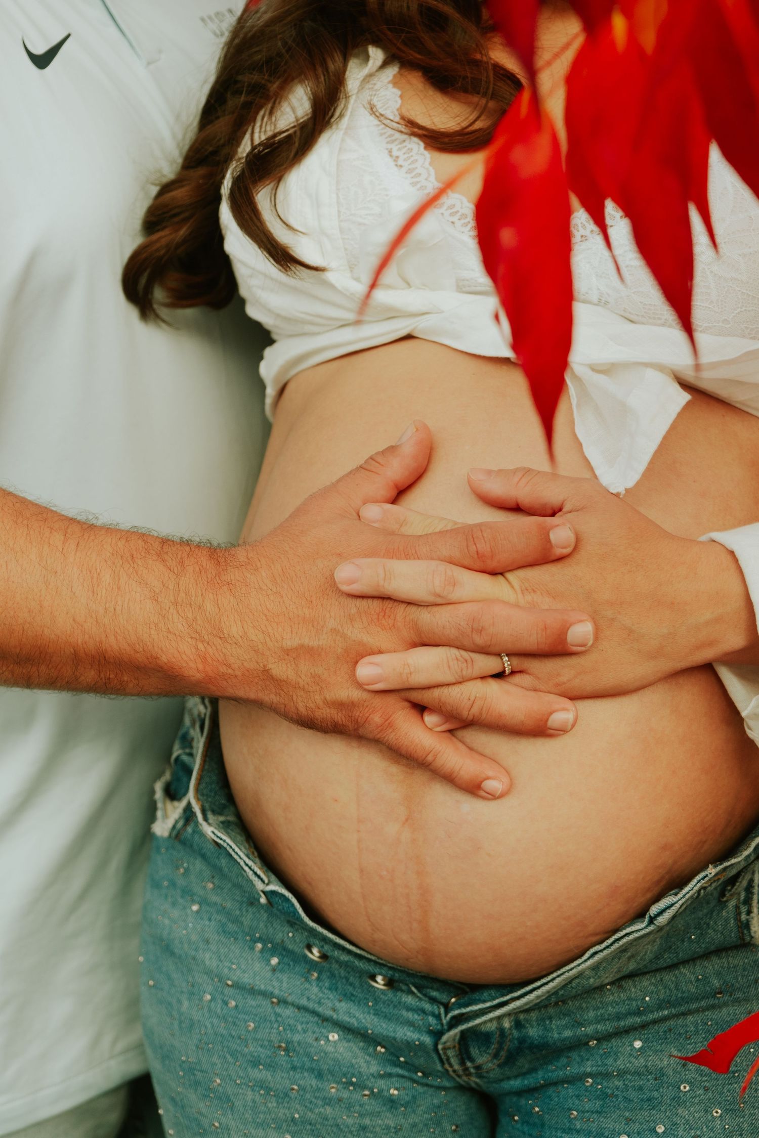 Close-up of hands tenderly touching a pregnant belly with red autumn leaves.