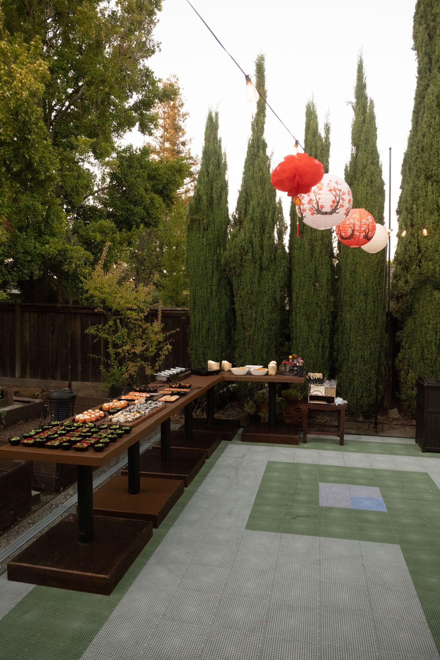 Modern outdoor patio with cypress trees and red paper lanterns at dusk.