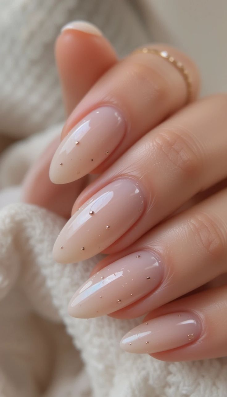 Elegant nude pink manicured nails with tiny sparkle details on a soft white fabric background.