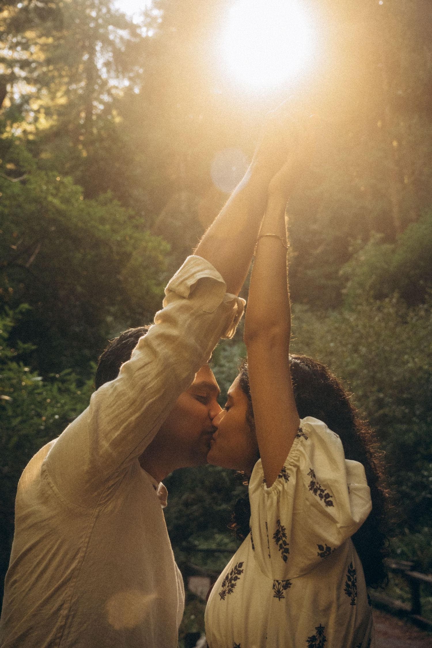 A couple shares a tender embrace against a sunlit forest backdrop in a romantic moment.